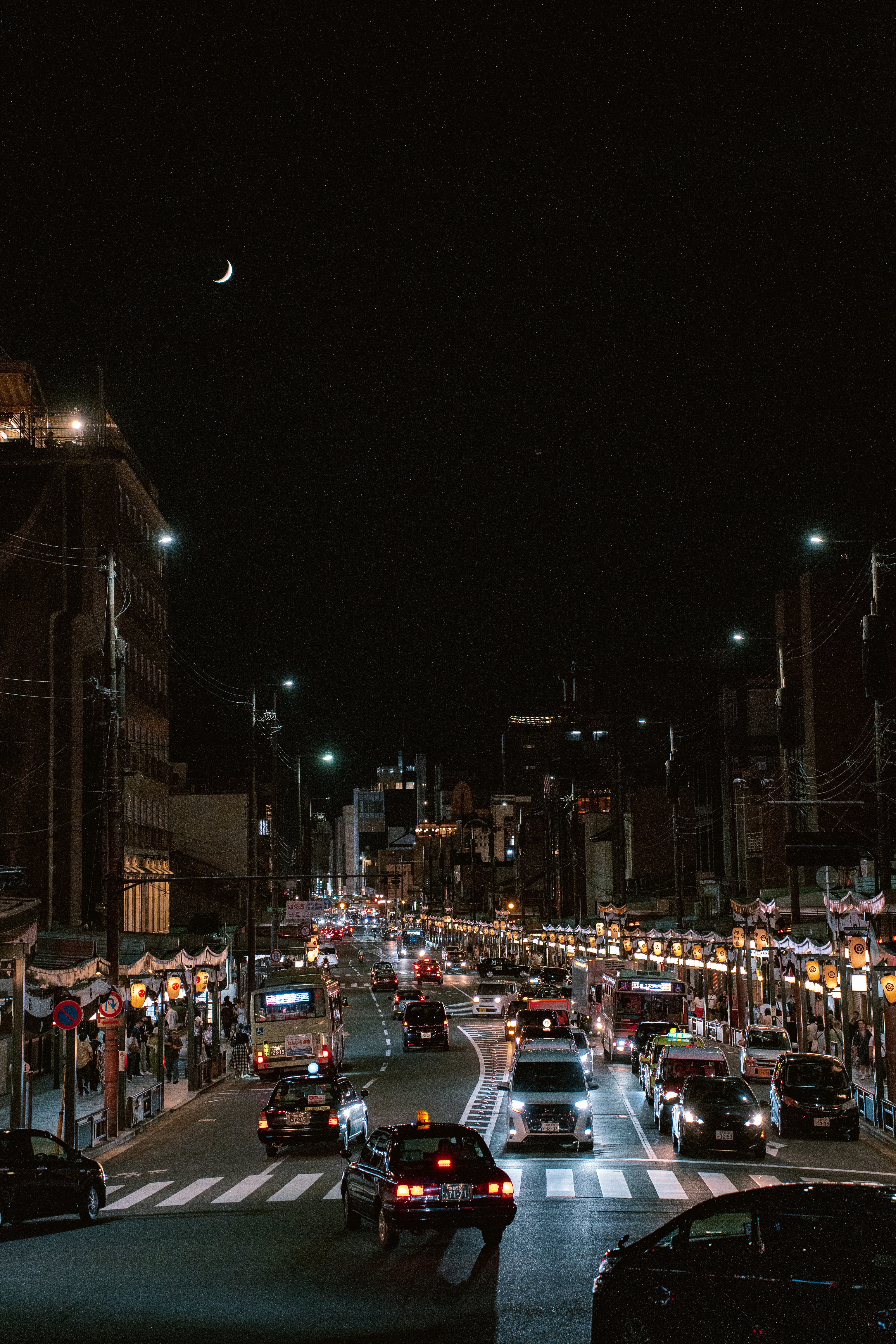 Nighttime city street with traffic and a crescent moon.