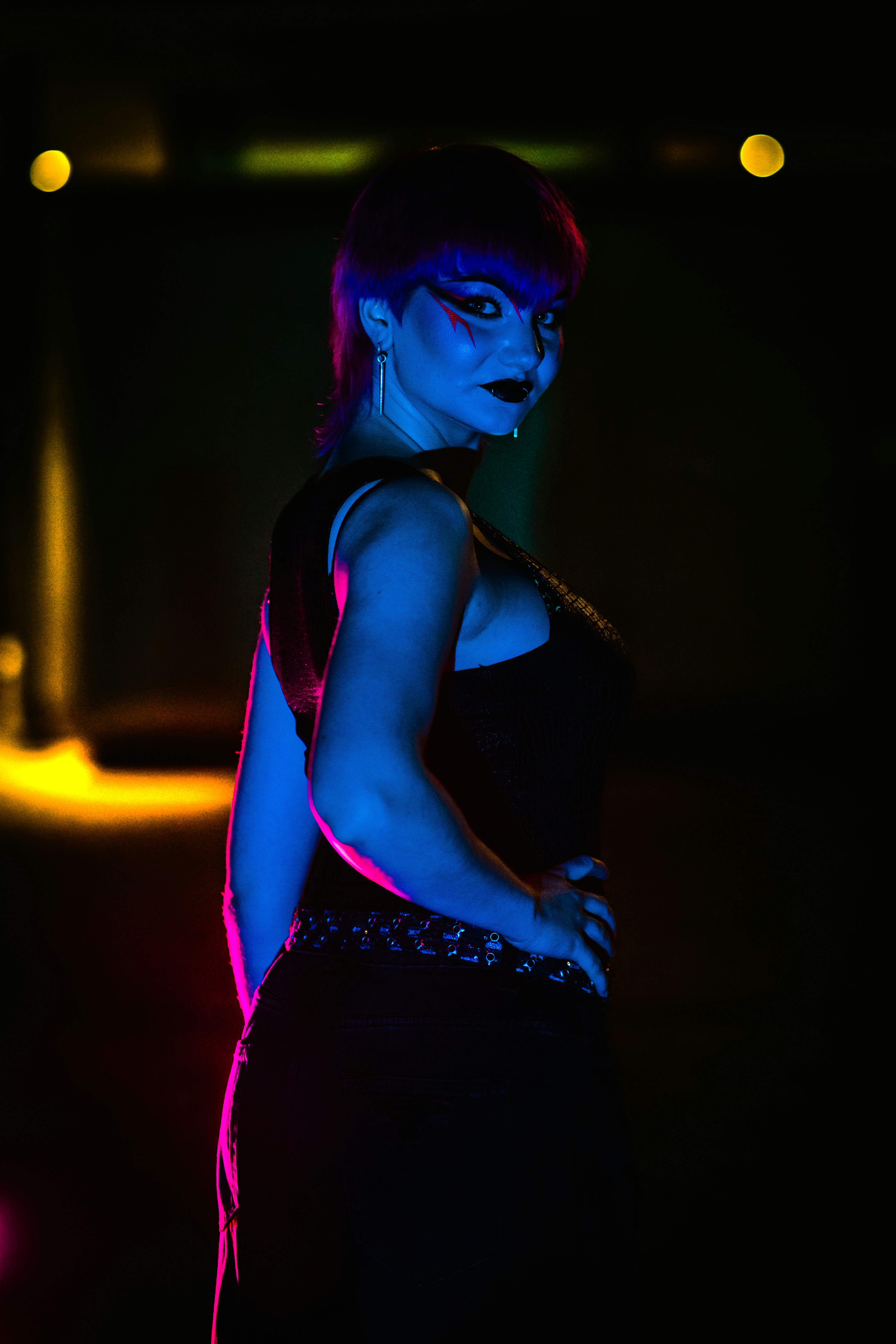 Wanita dengan riasan dramatis berpose di bawah lampu neon yang cerah.