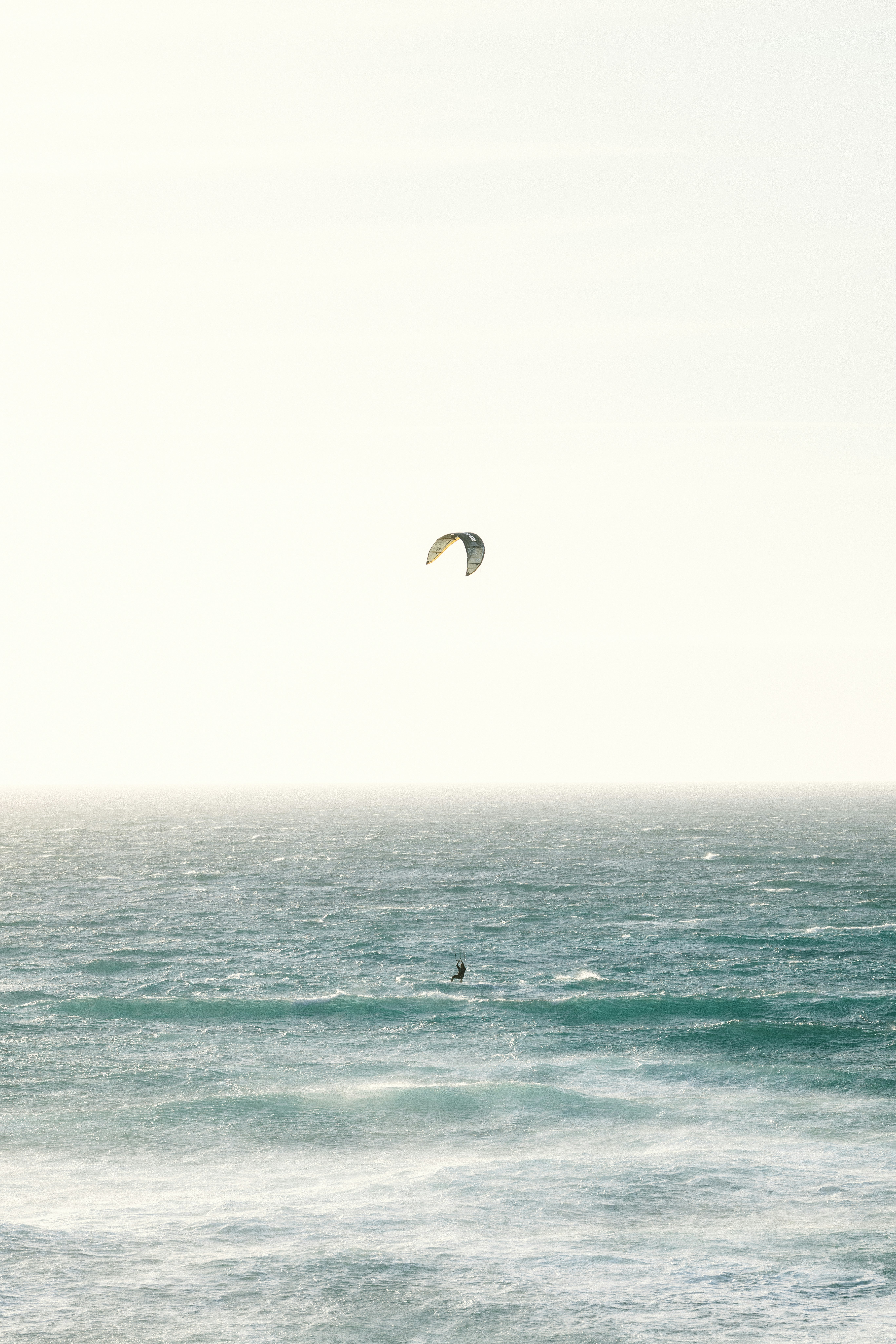 A person kitesurfing on the vast, hazy ocean.
