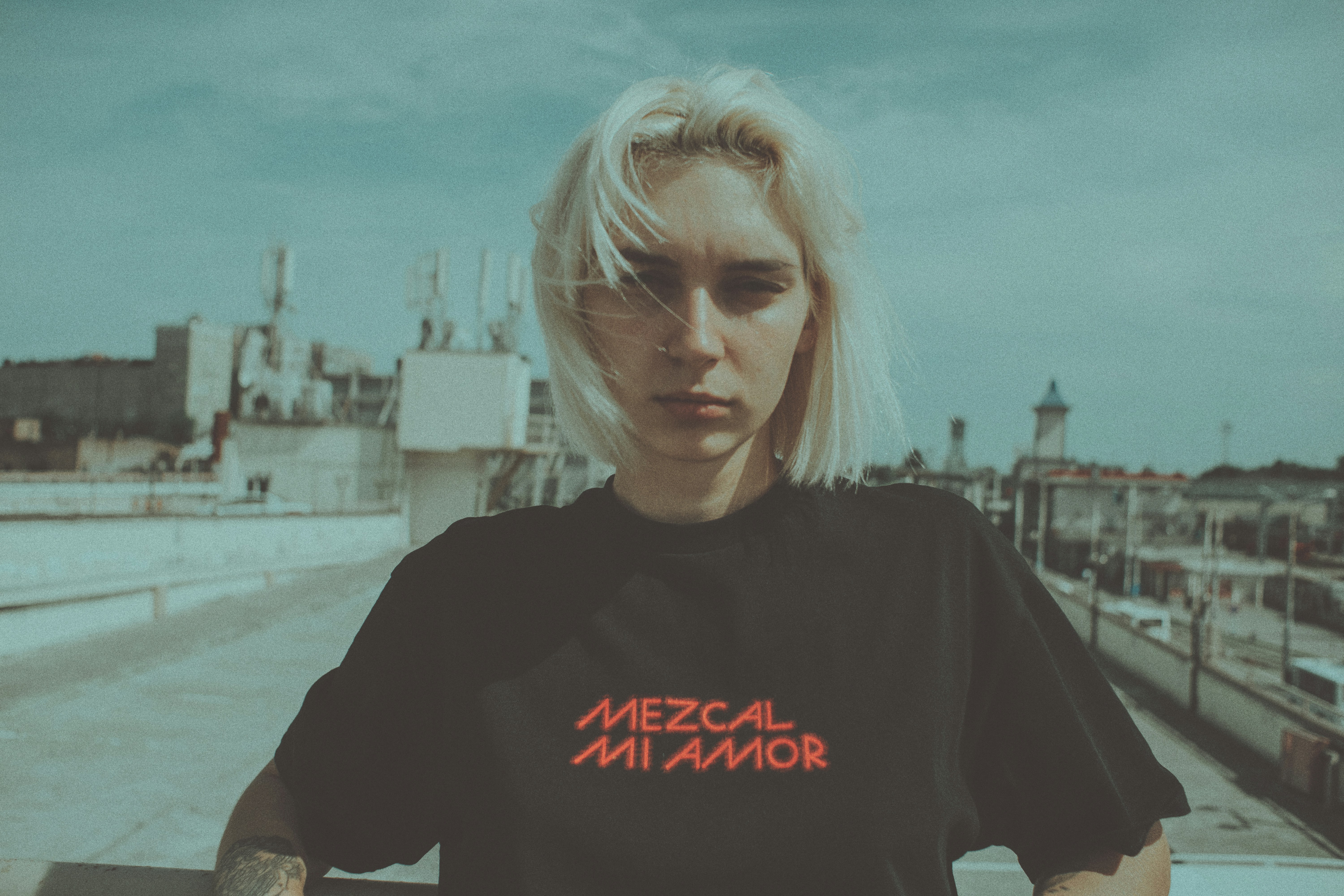 Blonde woman in black t-shirt looking at camera on rooftop