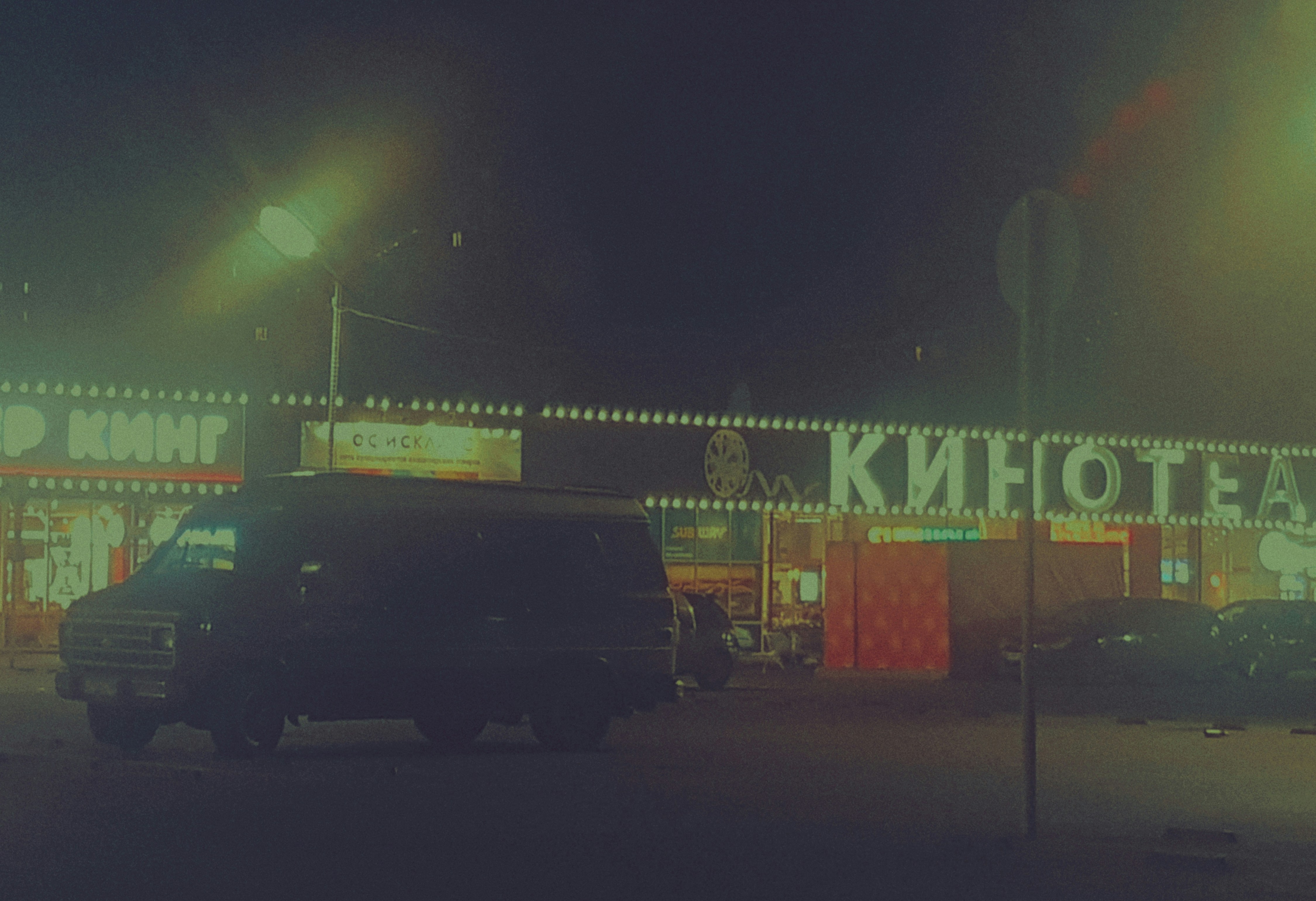 Night scene with a dark van and illuminated cinema building.