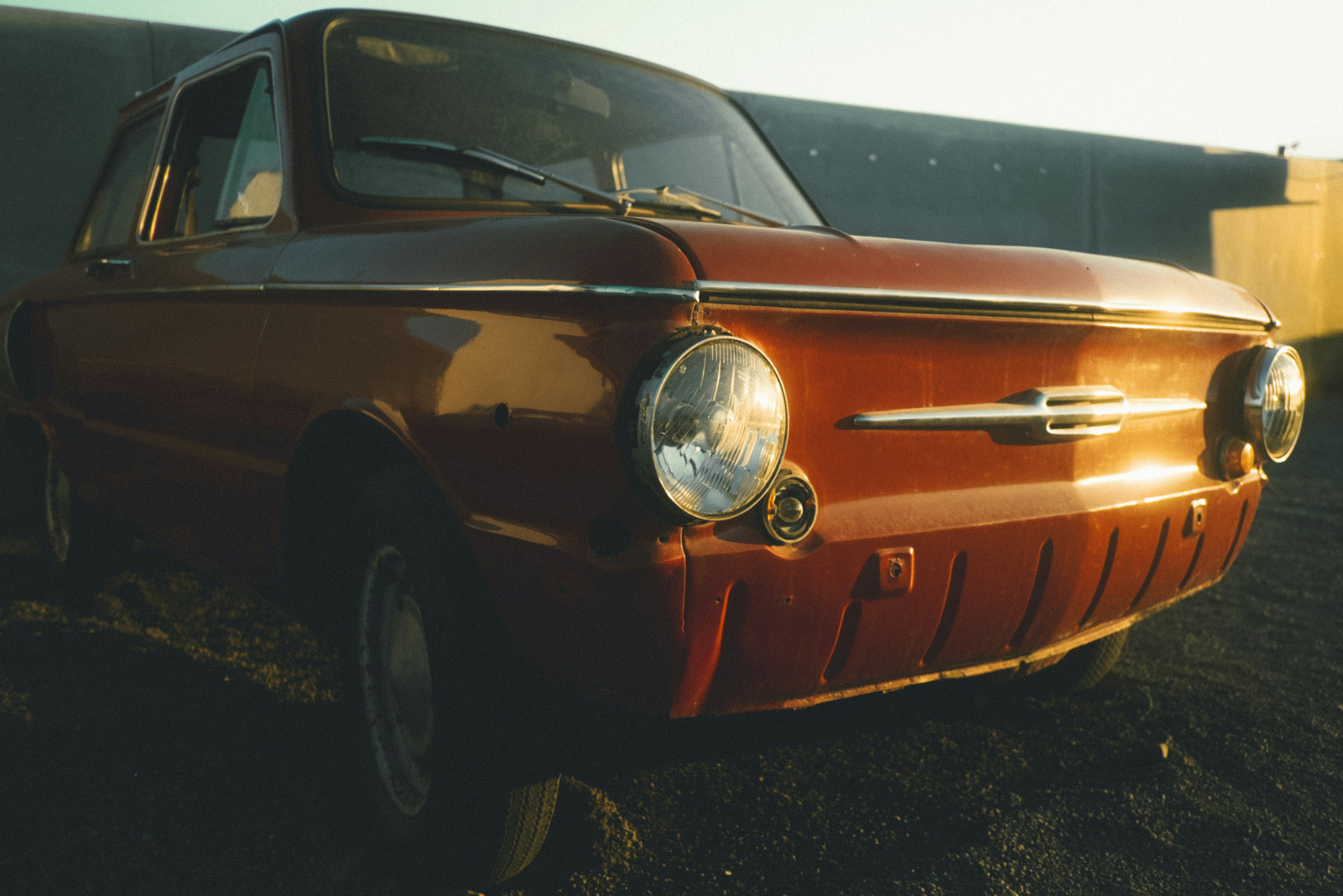 An old reddish-brown car parked outdoors in golden hour light.