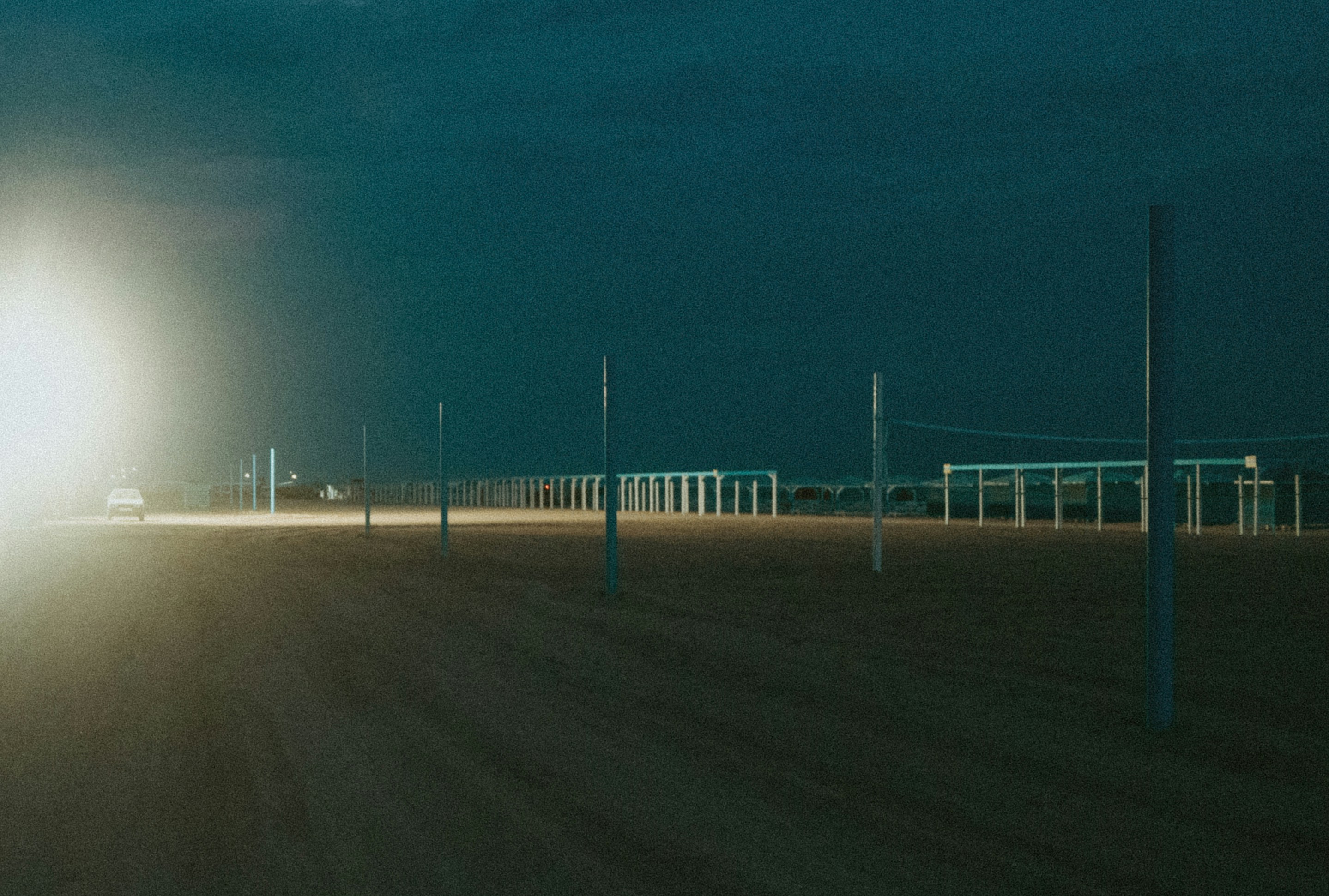 Bright light illuminates a dark, empty beach with poles.