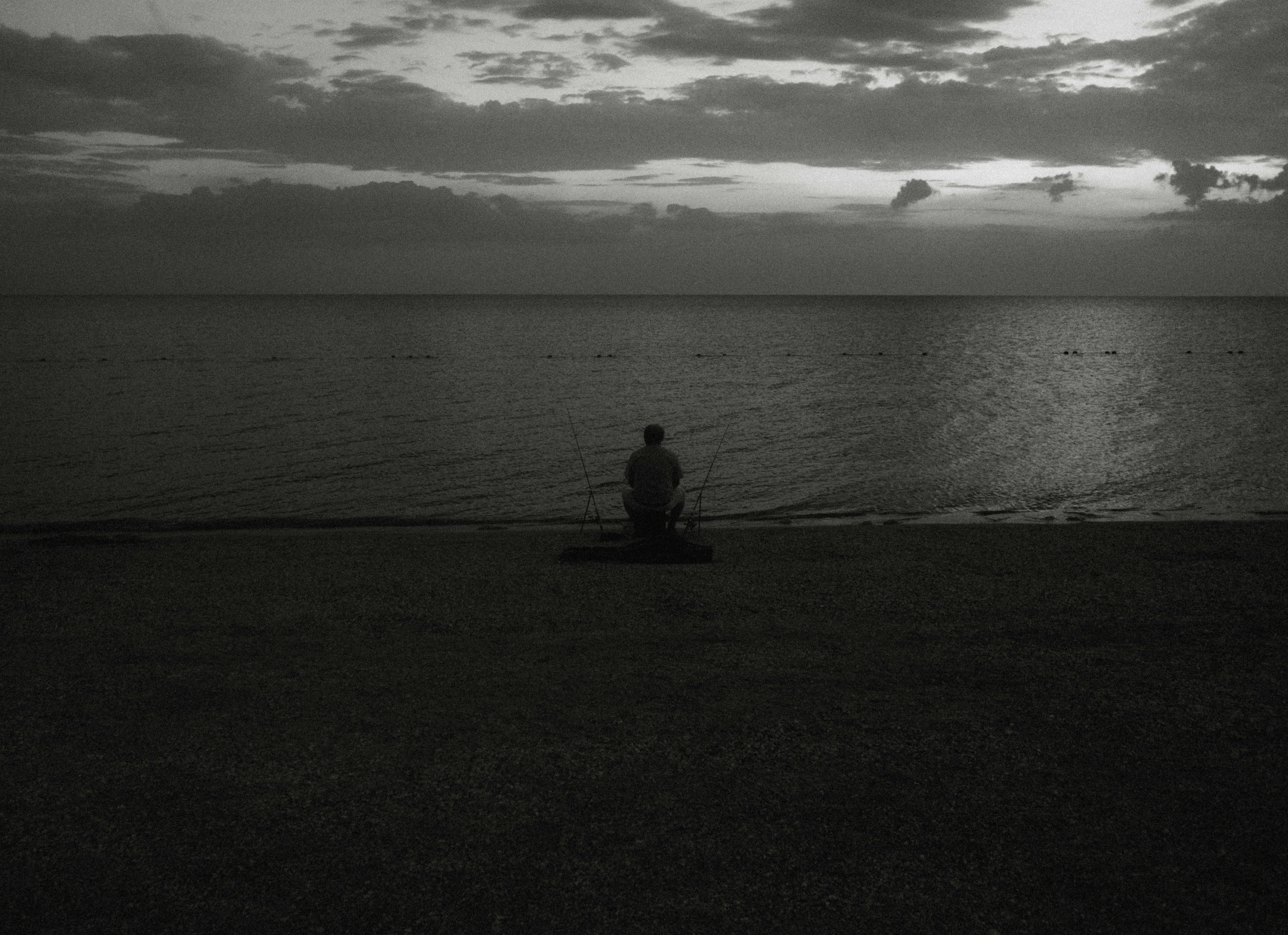Person sits on dark beach watching ocean at dusk.