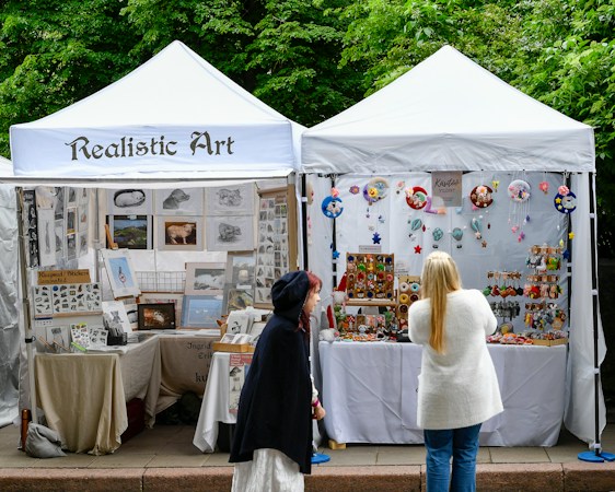 Two shoppers looking at handmade art and crafts displayed at an outdoor market booth