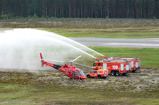 Fire truck douses a red helicopter with water.