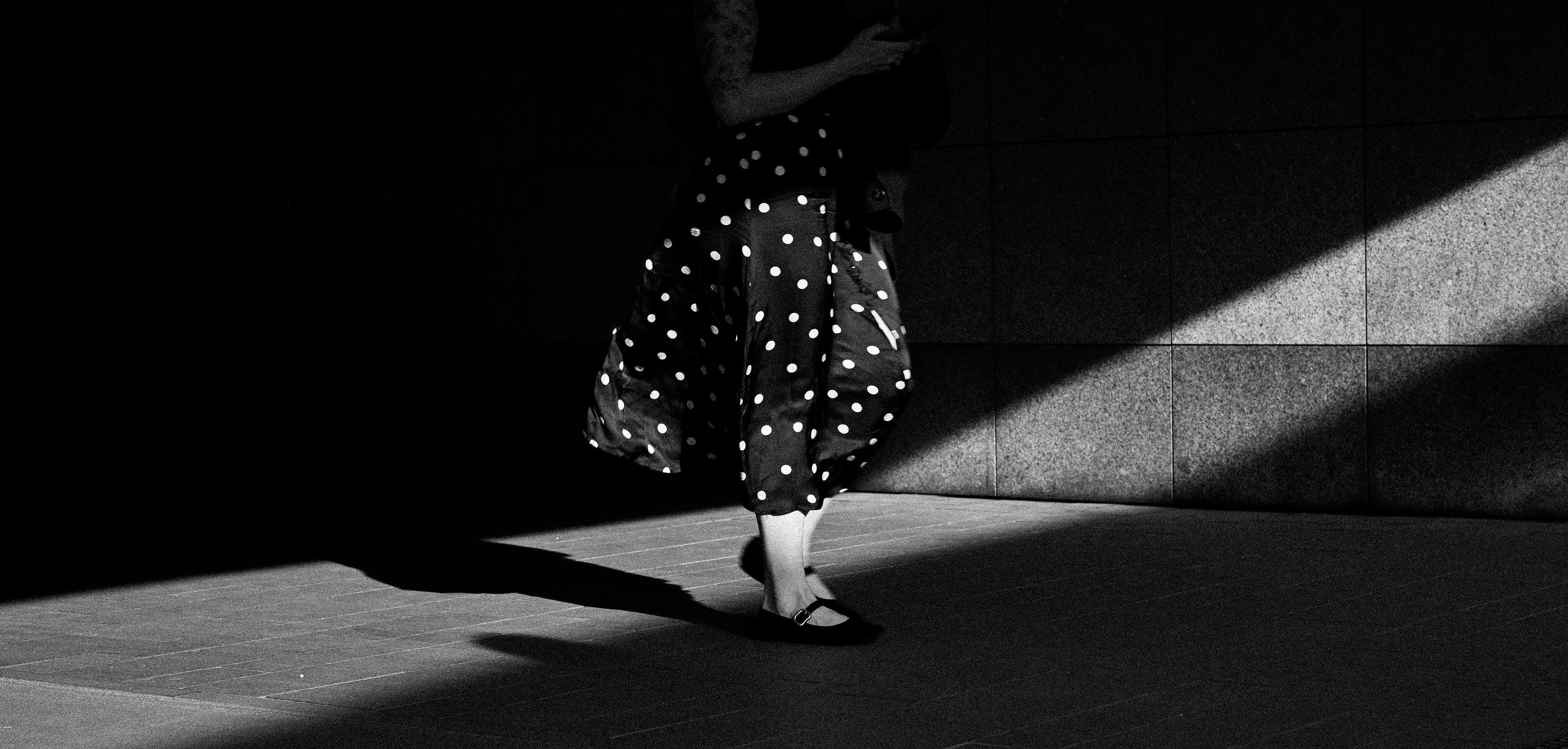 Person in polka dot skirt walking through light and shadow.