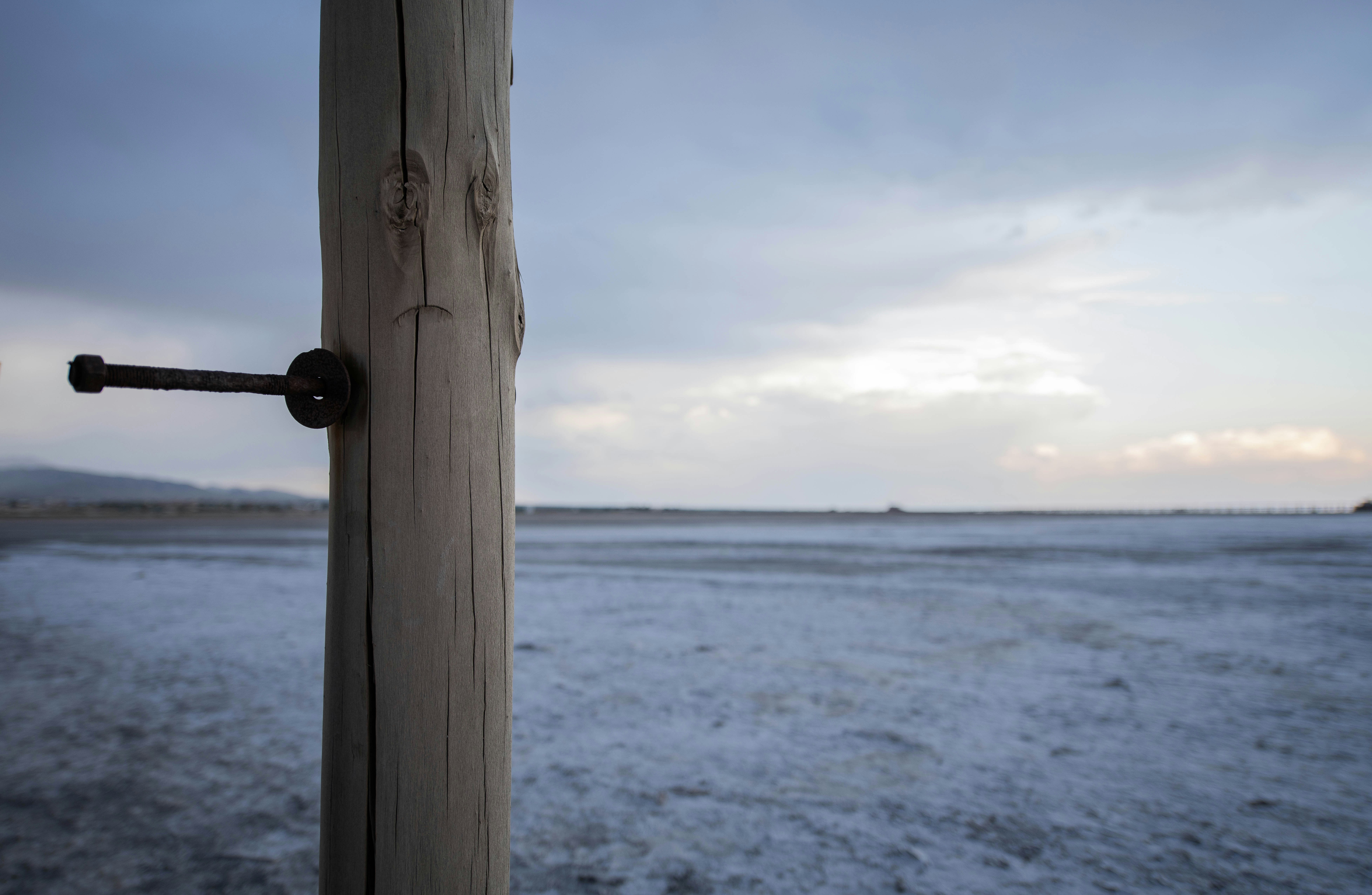 Holzpfosten mit Bolzen, verschneite Landschaft und bewölkter Himmel.