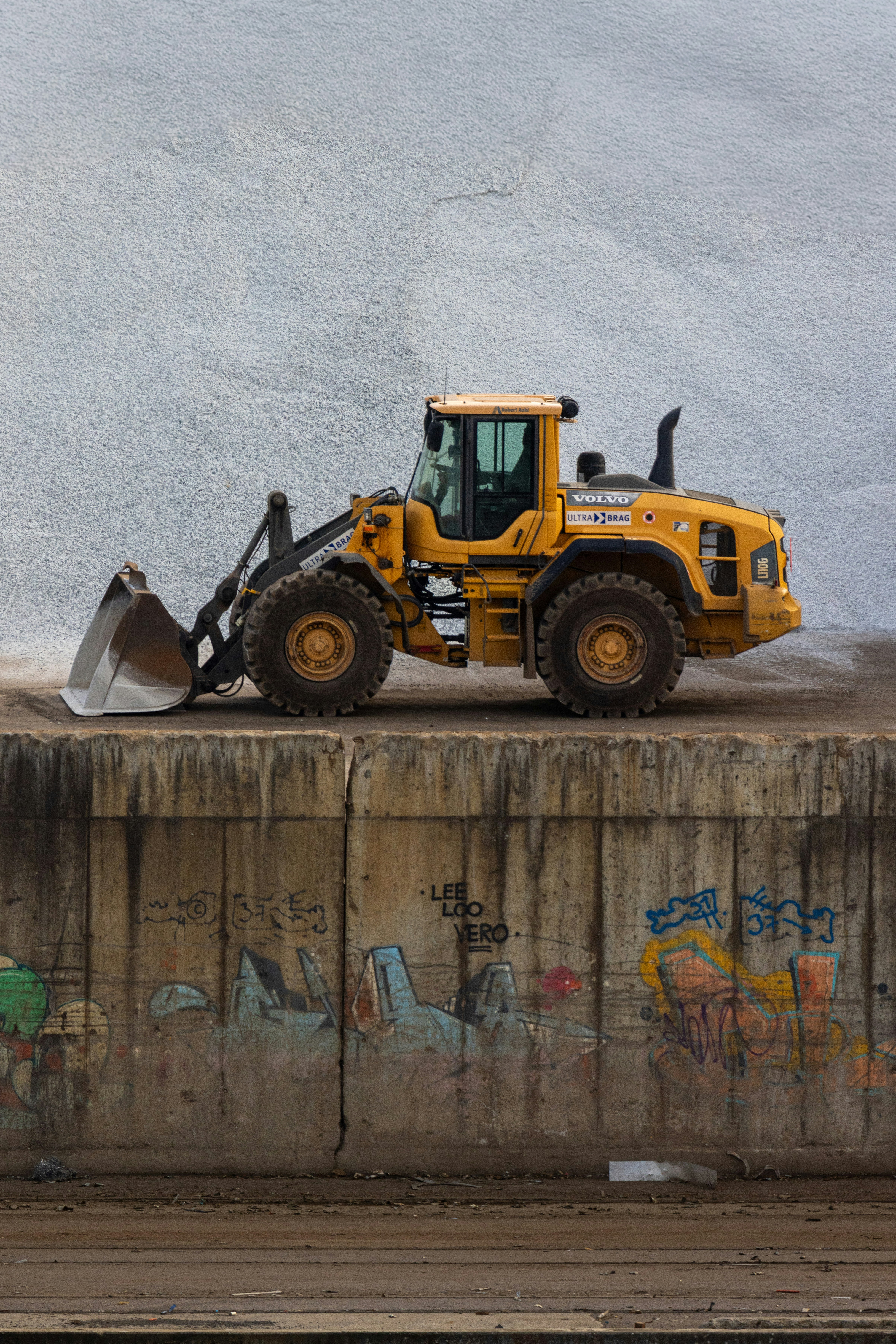 Yellow front-end loader on concrete barrier with large white pile.