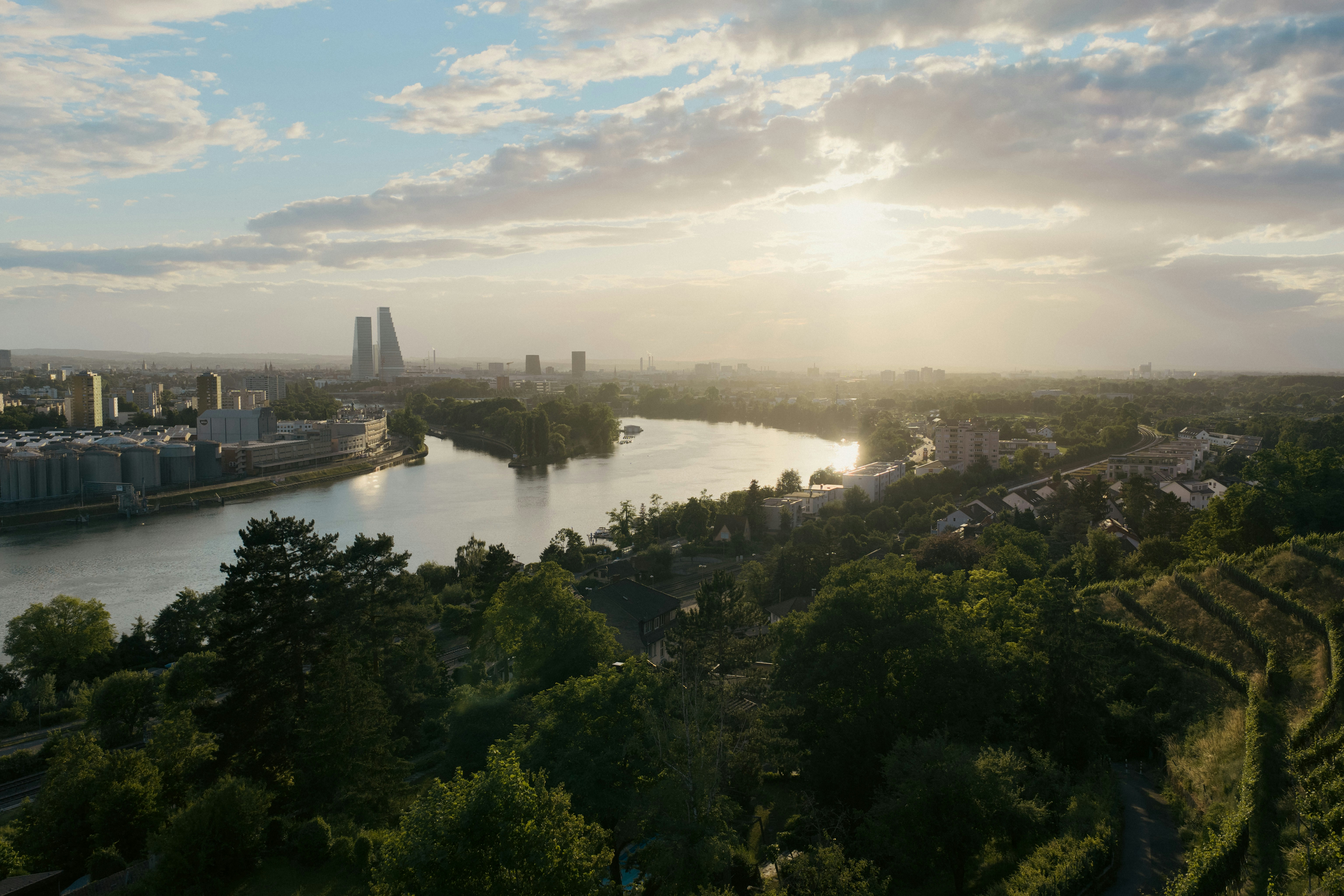 City skyline and river at sunset with lush green trees.