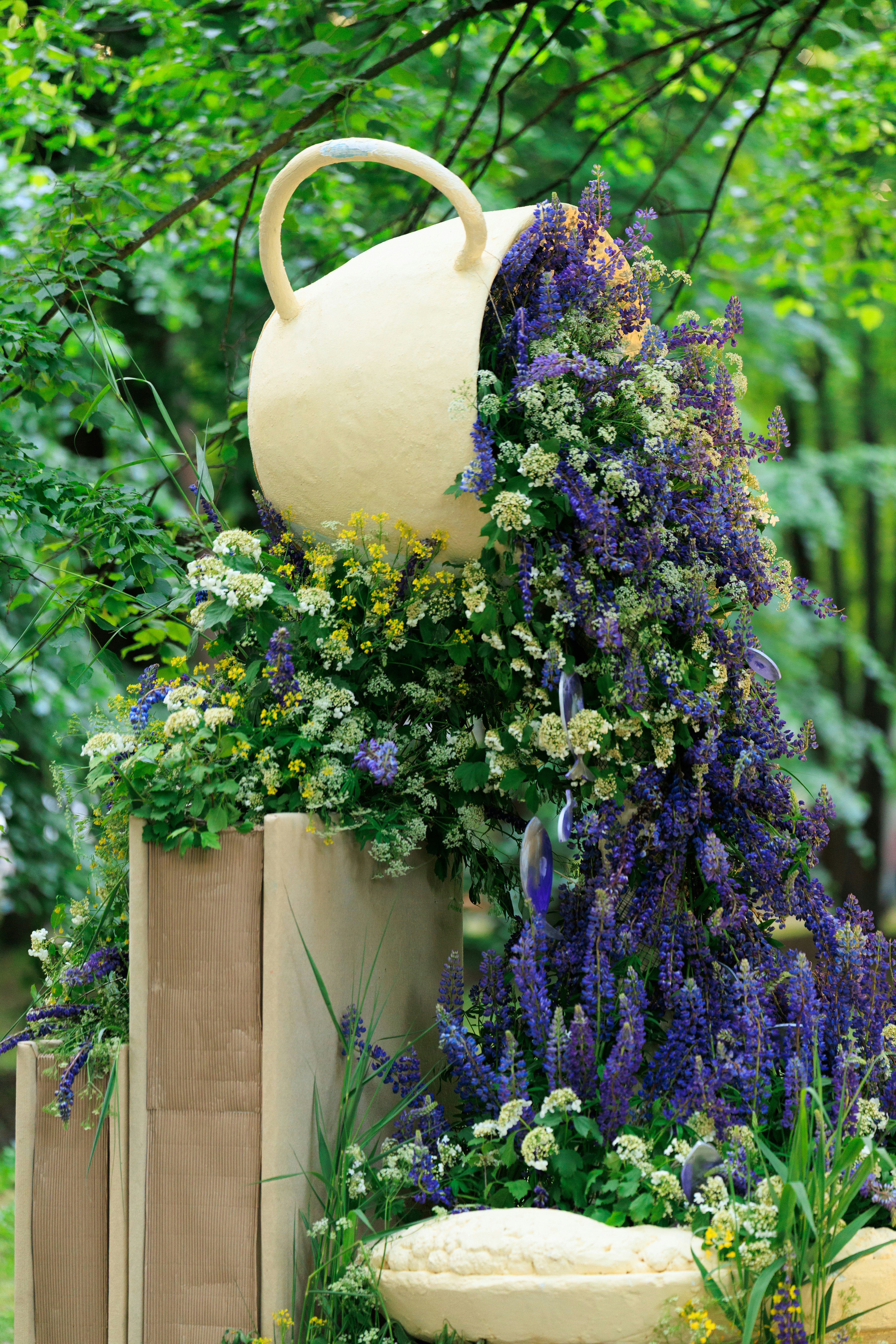 Giant teacup spilling purple flowers and green foliage in garden.