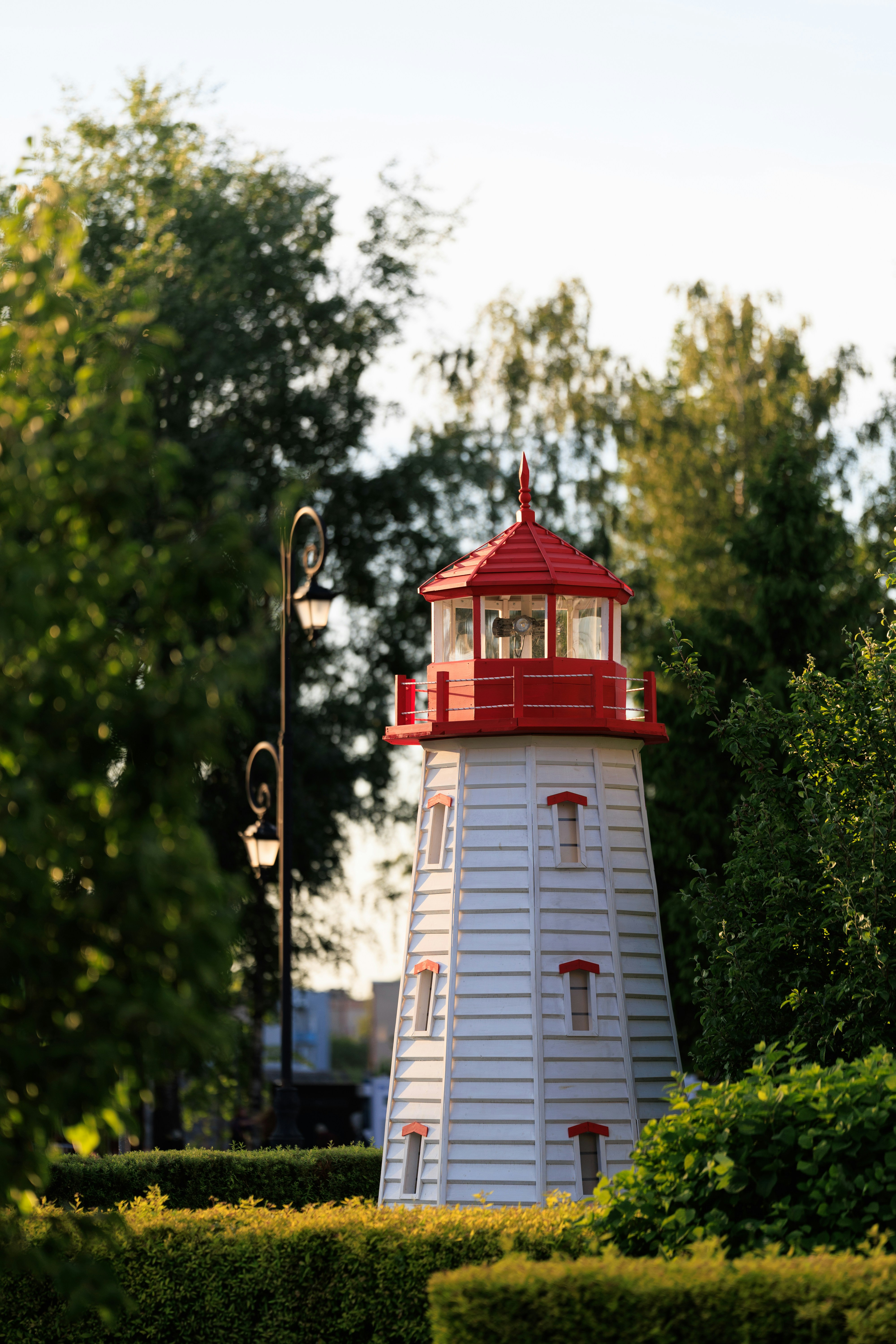 A charming white and red lighthouse in a green park.