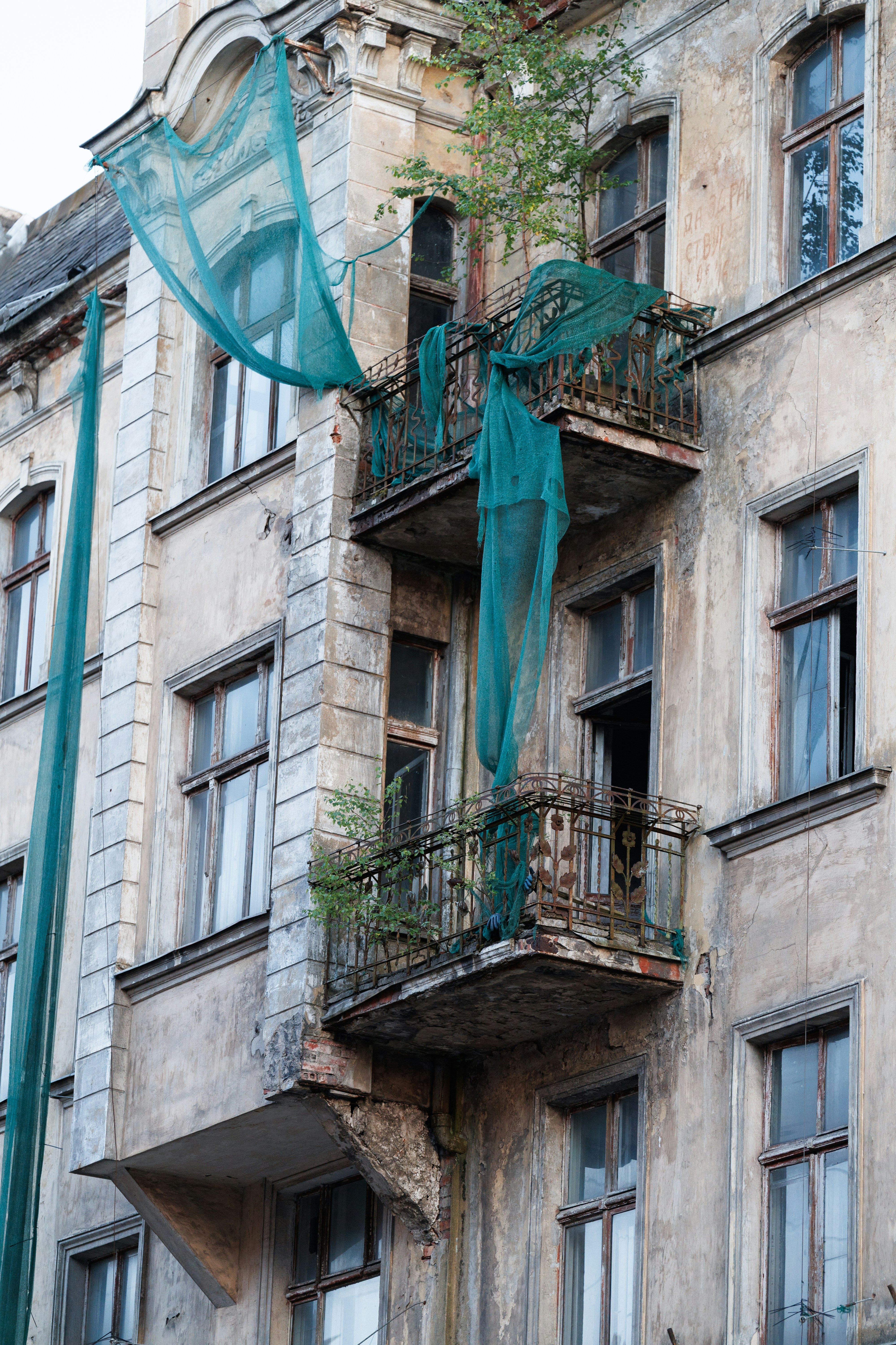 Dilapidated building with two balconies draped in green netting.