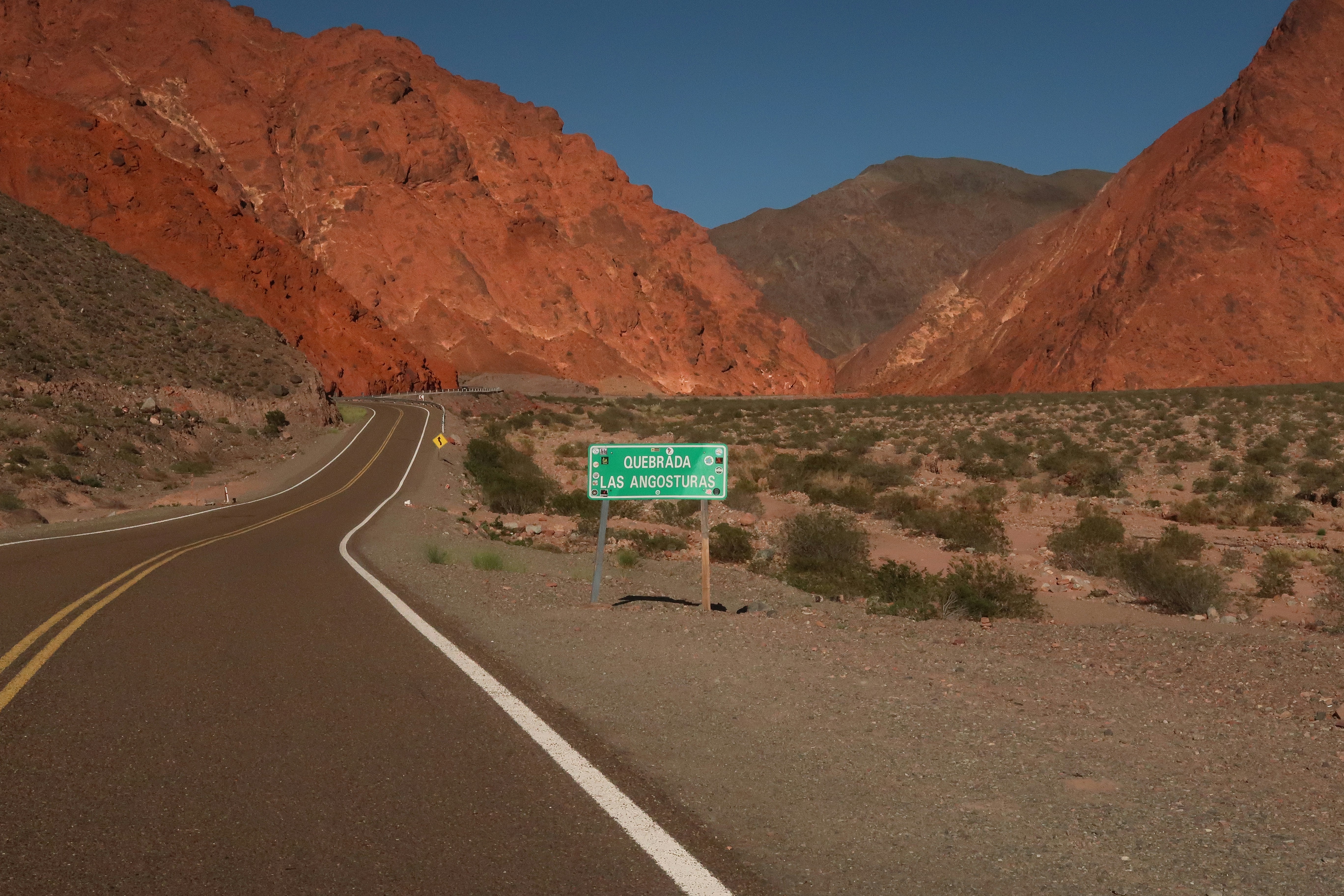 Road winding through red mountains with a green sign.