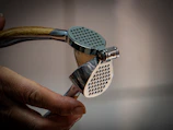Hand holding an open, metallic garlic press.
