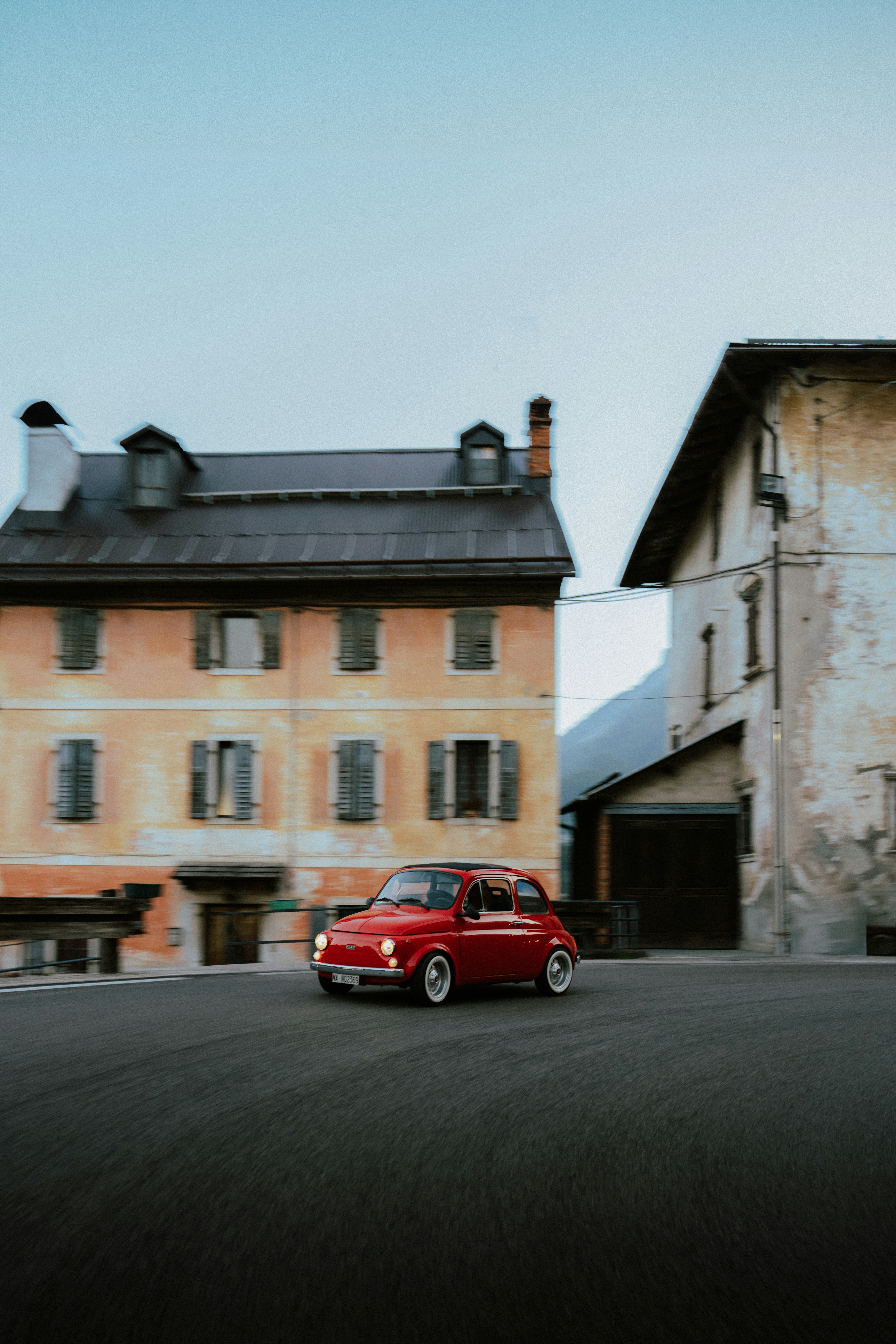 A red vintage car drives past old buildings.