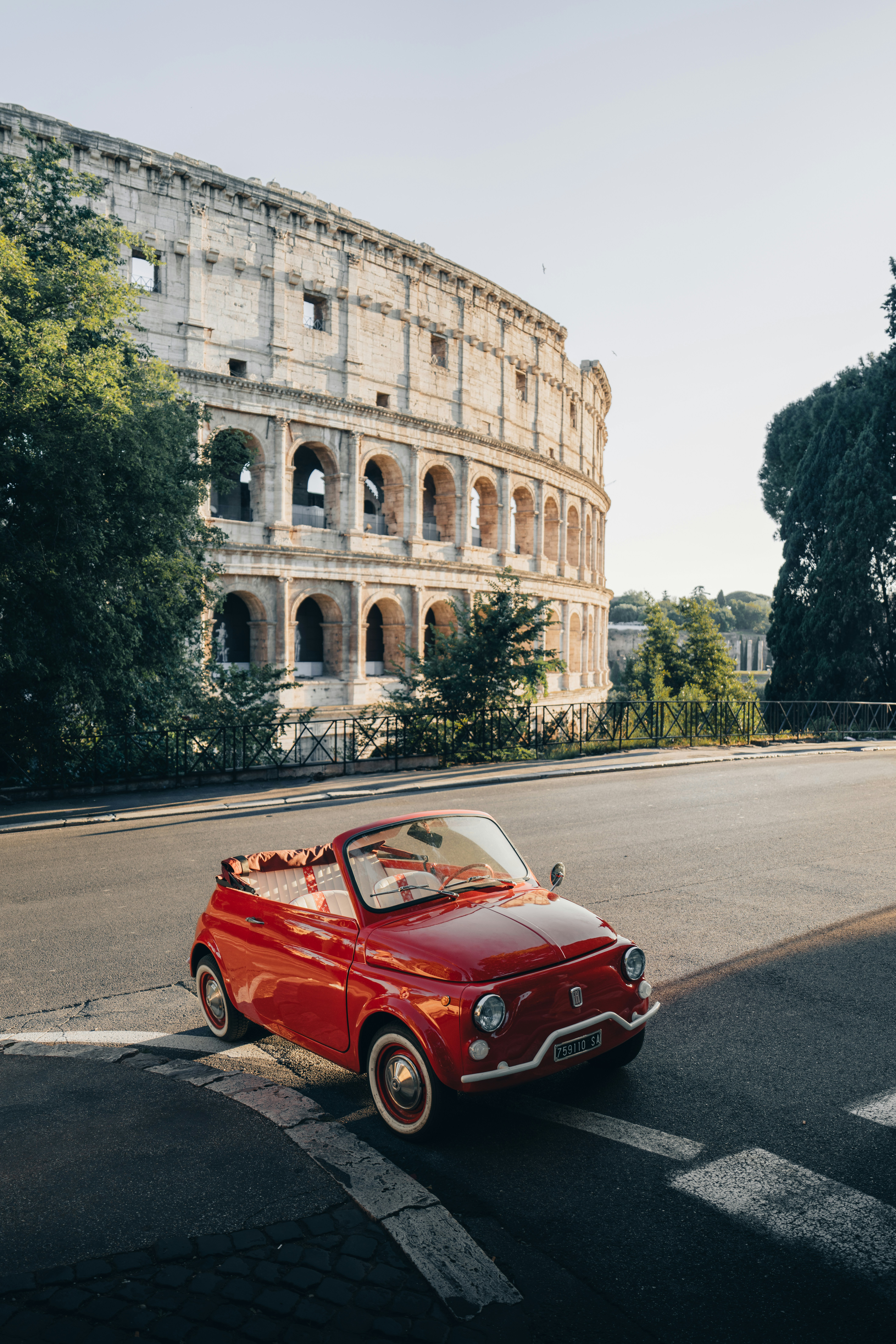 A red vintage car parked near the ancient roman colosseum.