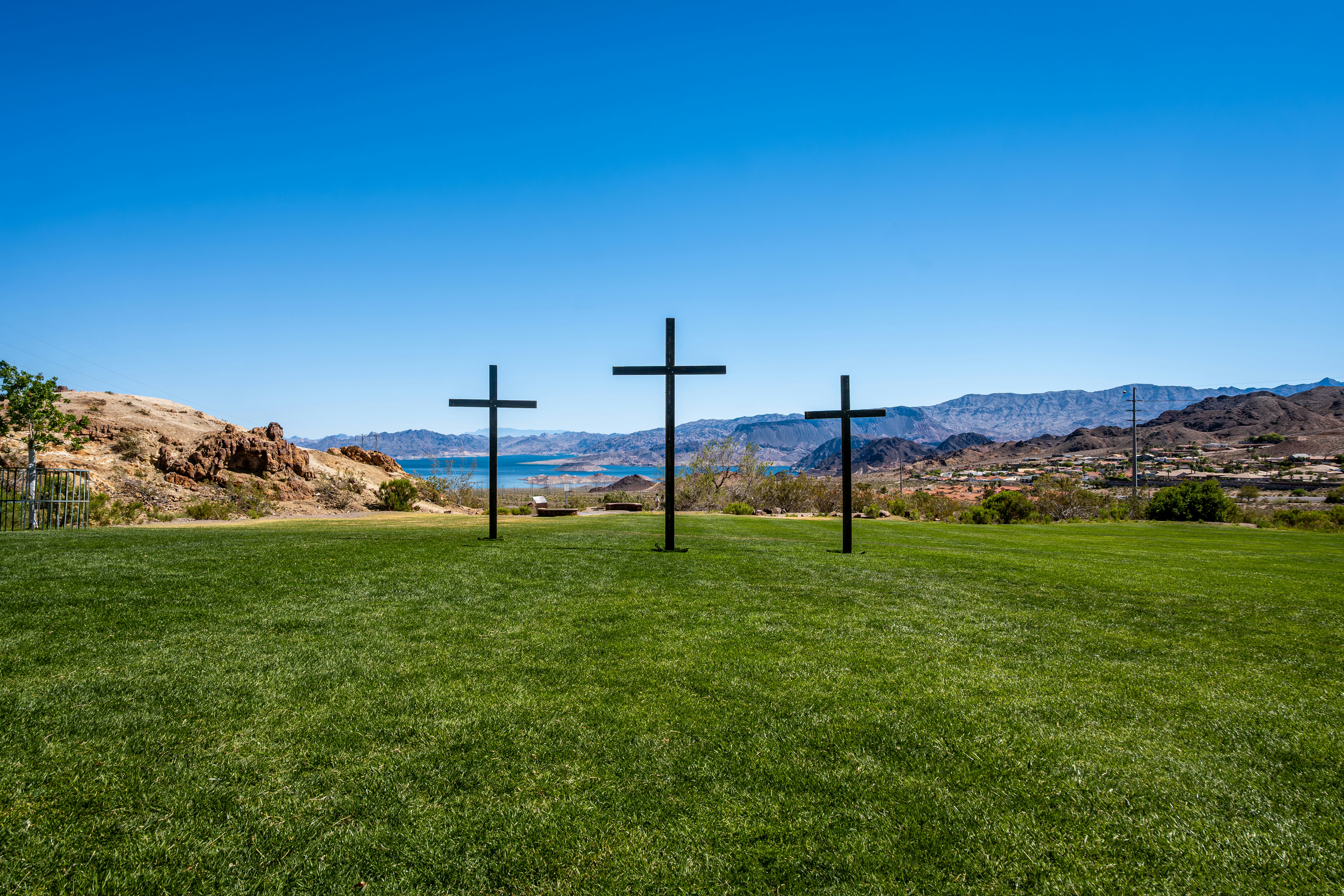 Three crosses on a grassy hill overlooking a lake.