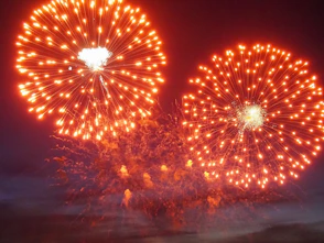 Two vibrant orange fireworks explode against a dark night sky.
