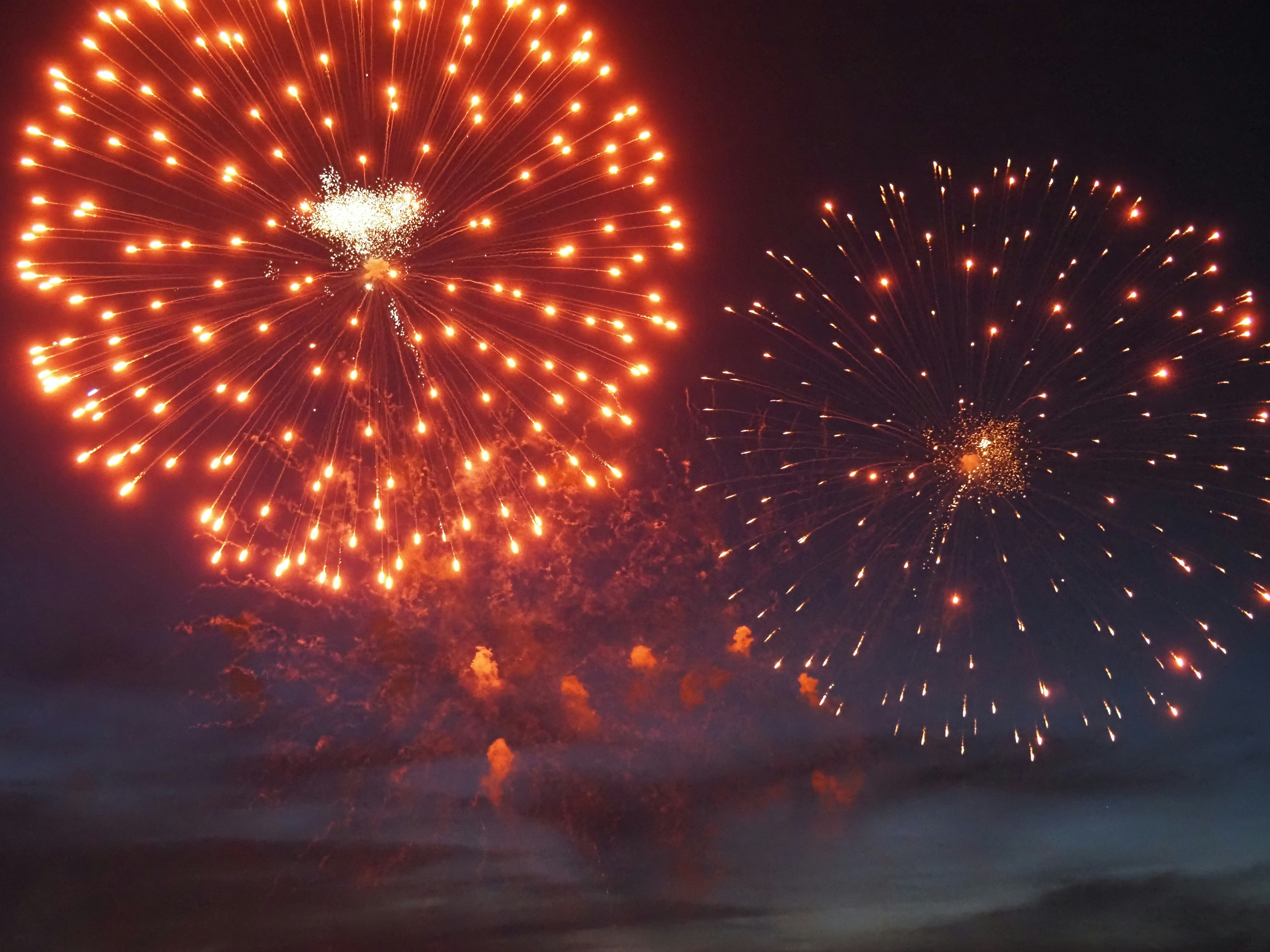Two vibrant orange fireworks explode against a dark night sky.