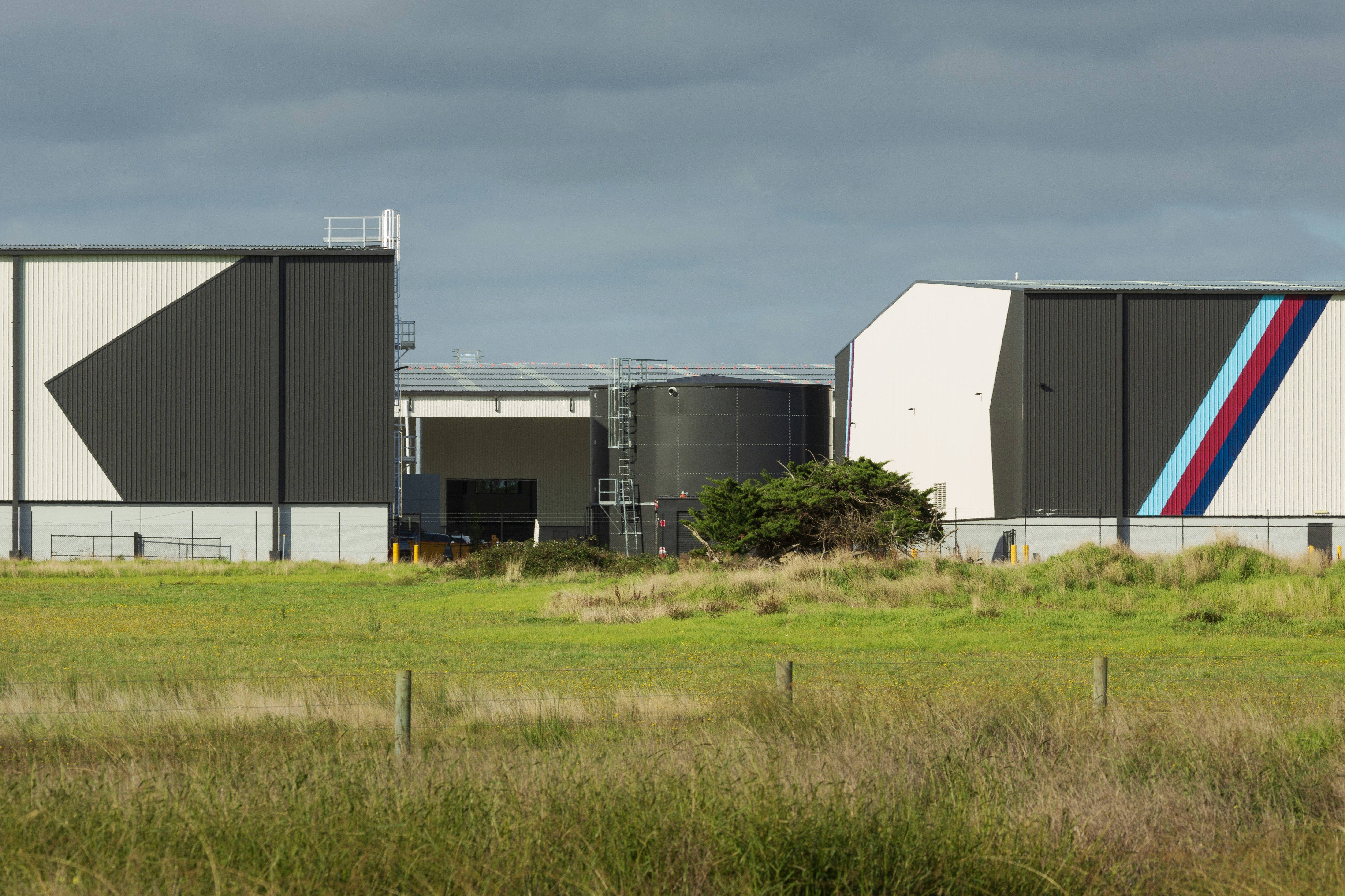 Modern industrial buildings with geometric patterns and a grassy field.