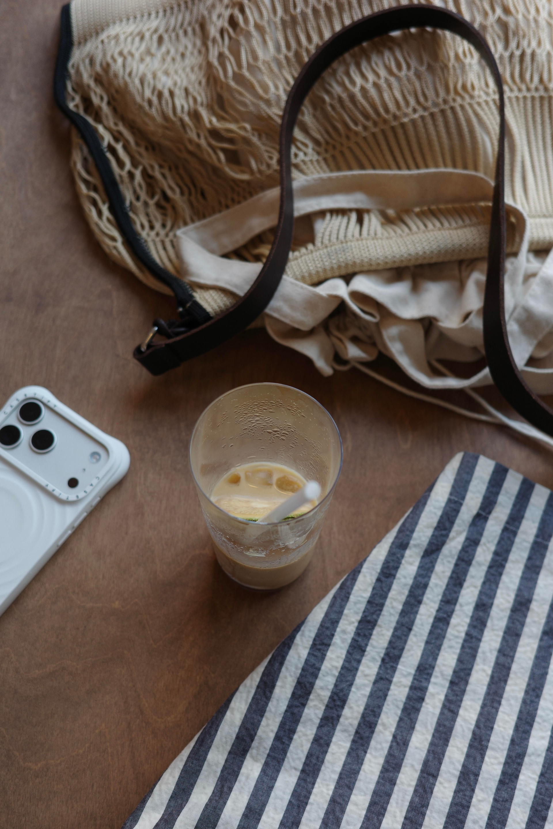 Iced coffee, white phone, beige bag, and striped cloth.