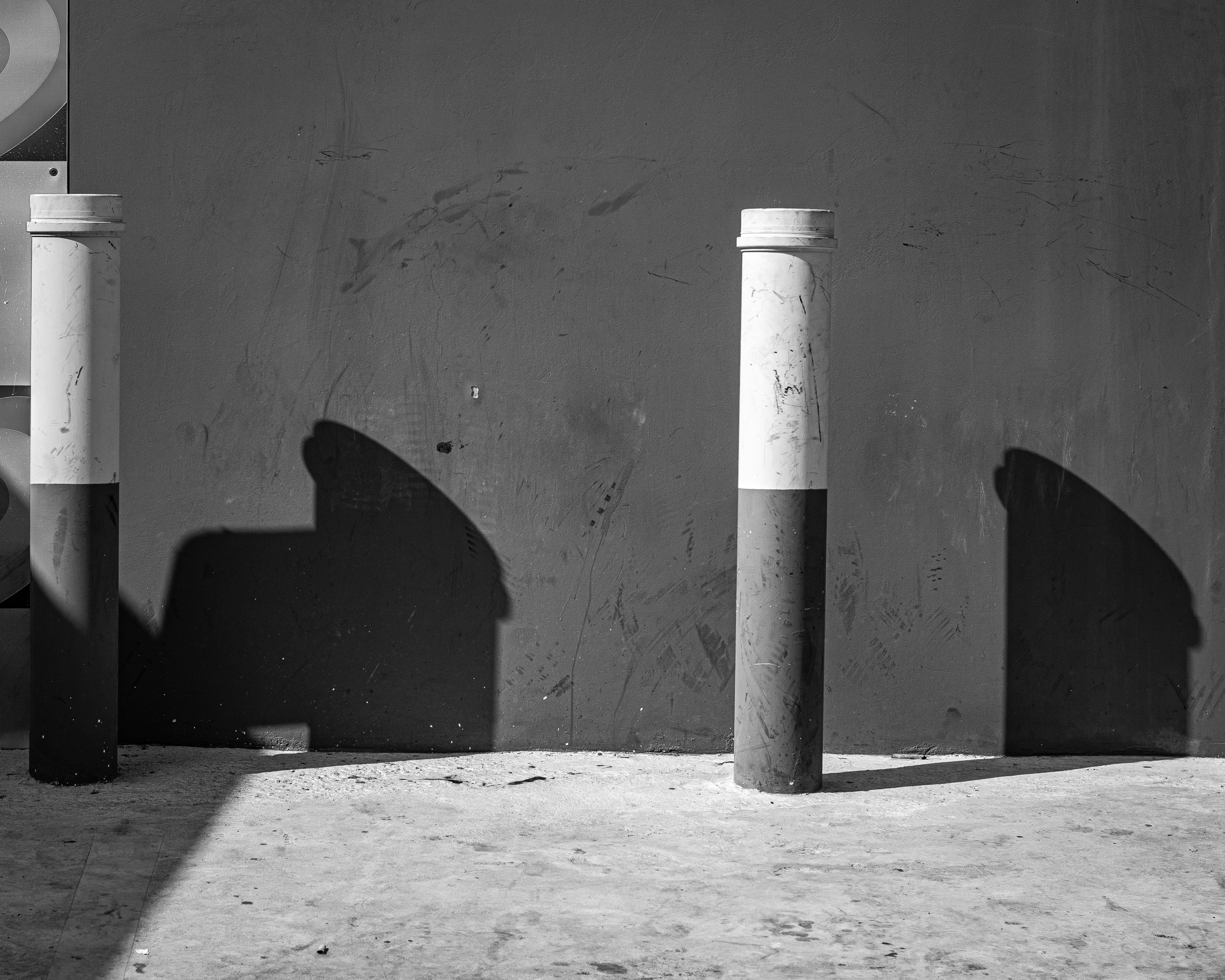 Two striped posts cast long shadows on a wall.