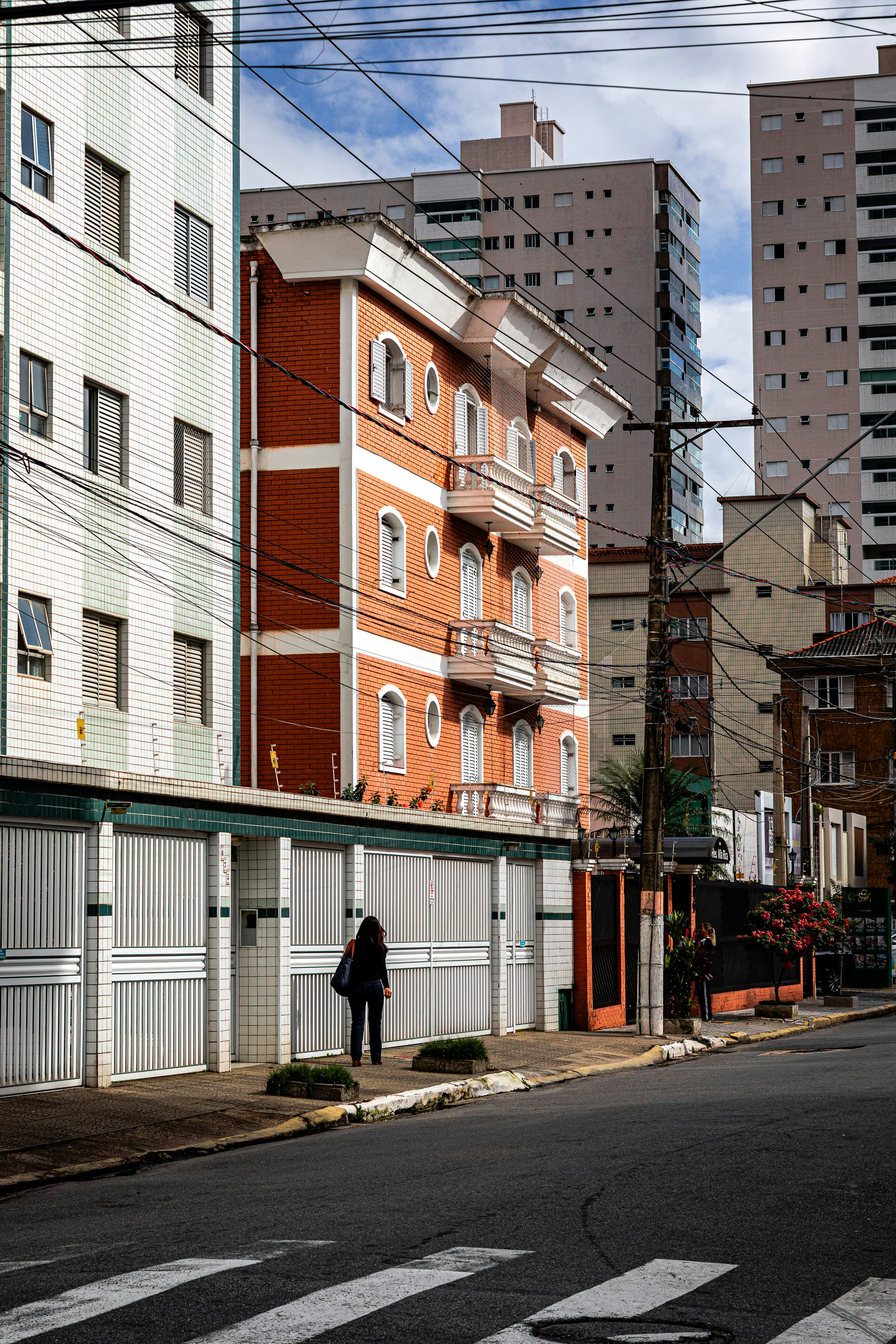 A woman stands on a sidewalk beside an orange building.
