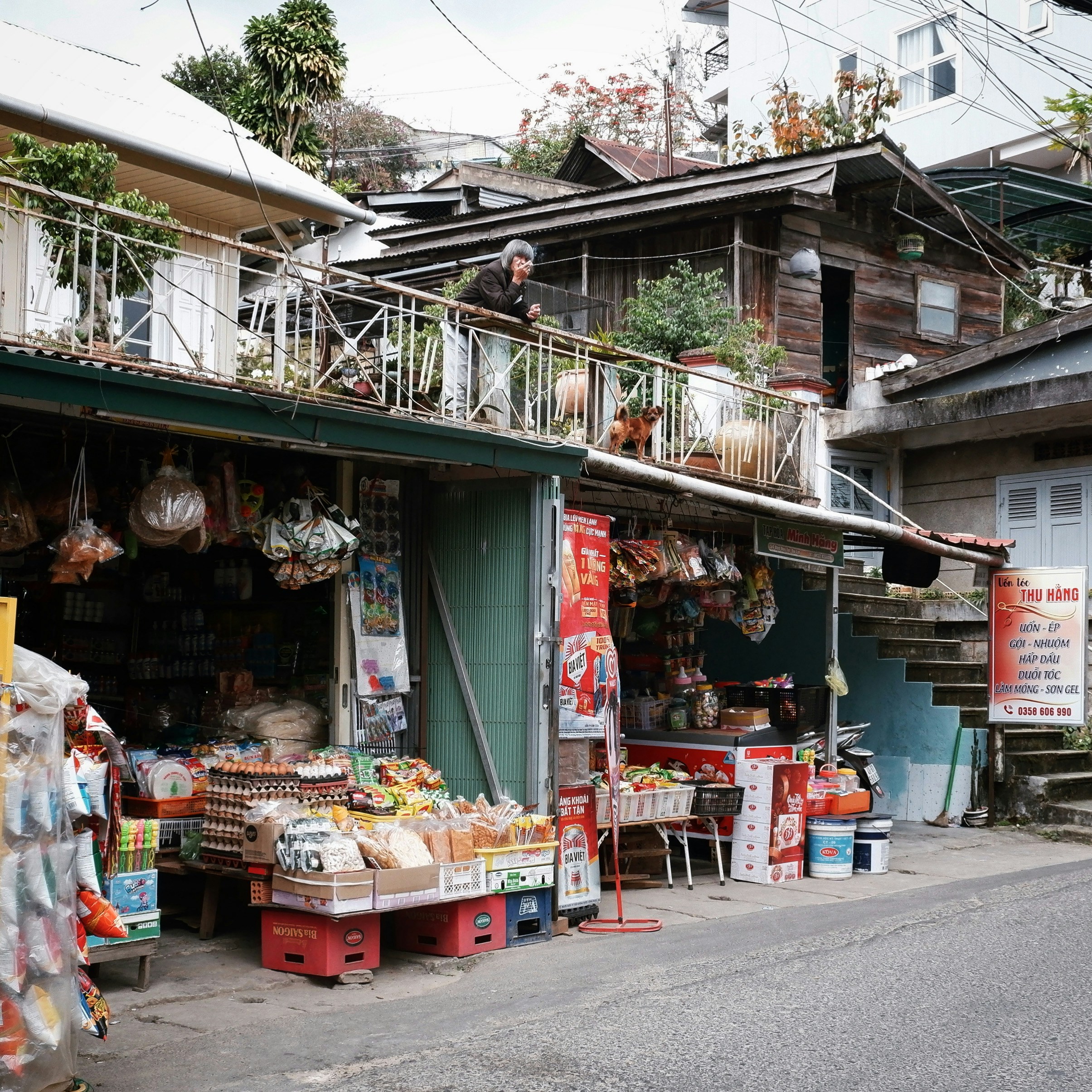 A person on a balcony overlooks bustling street shops.