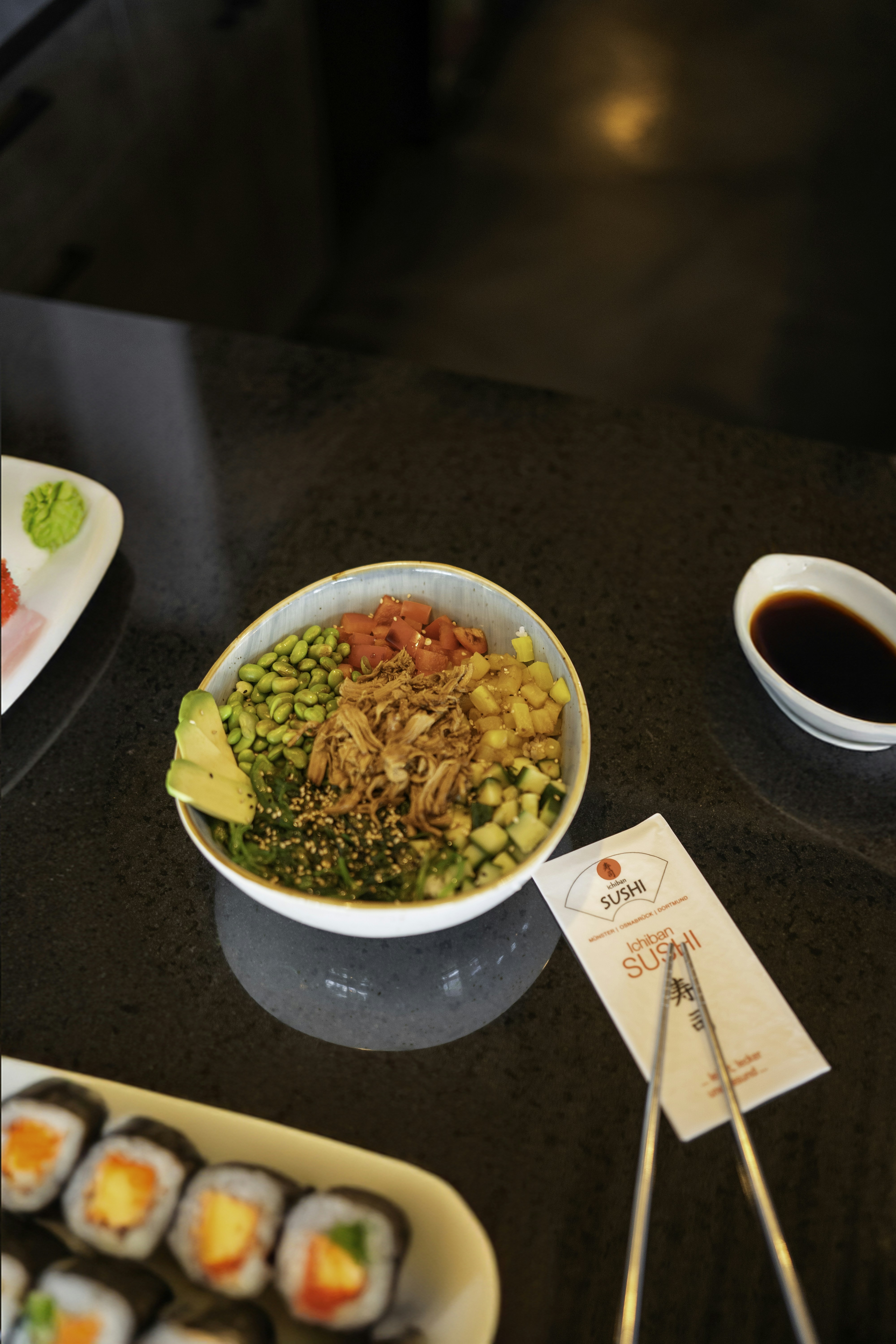 Fresh poke bowl and sushi rolls on a dark counter.
