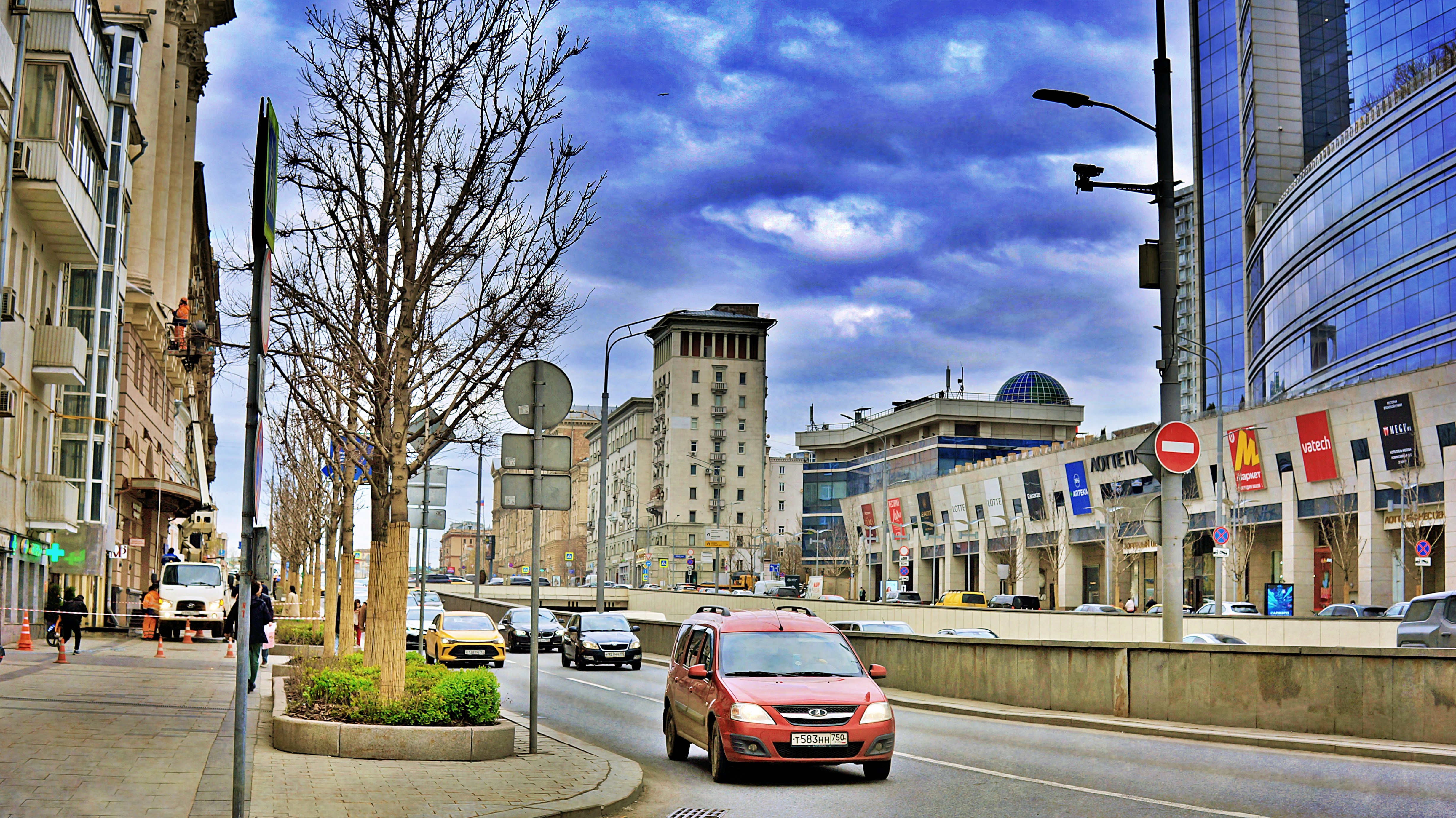 A city street with buildings, cars, and dramatic cloudy sky.