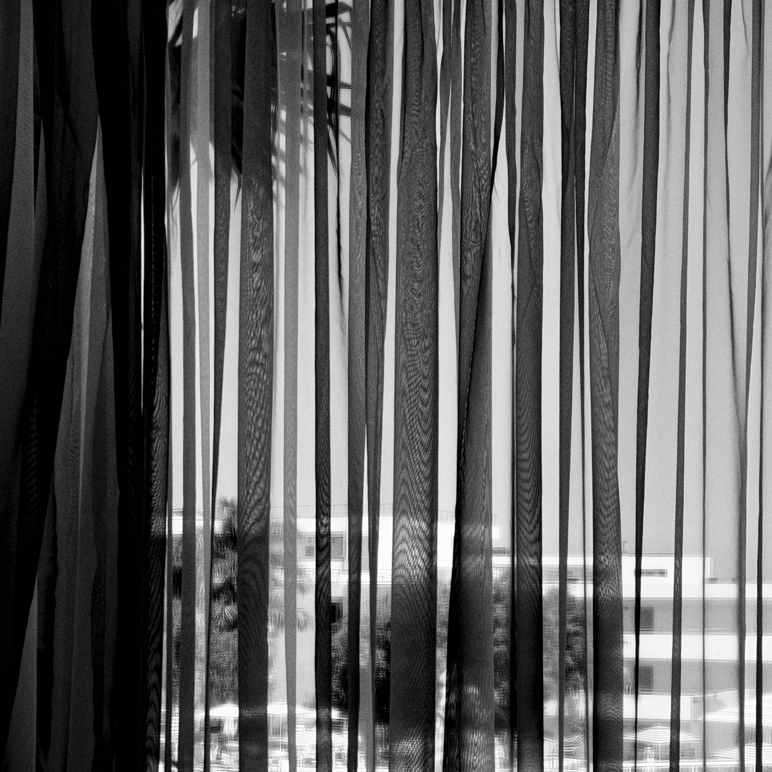 Black and white view through sheer vertical curtains.
