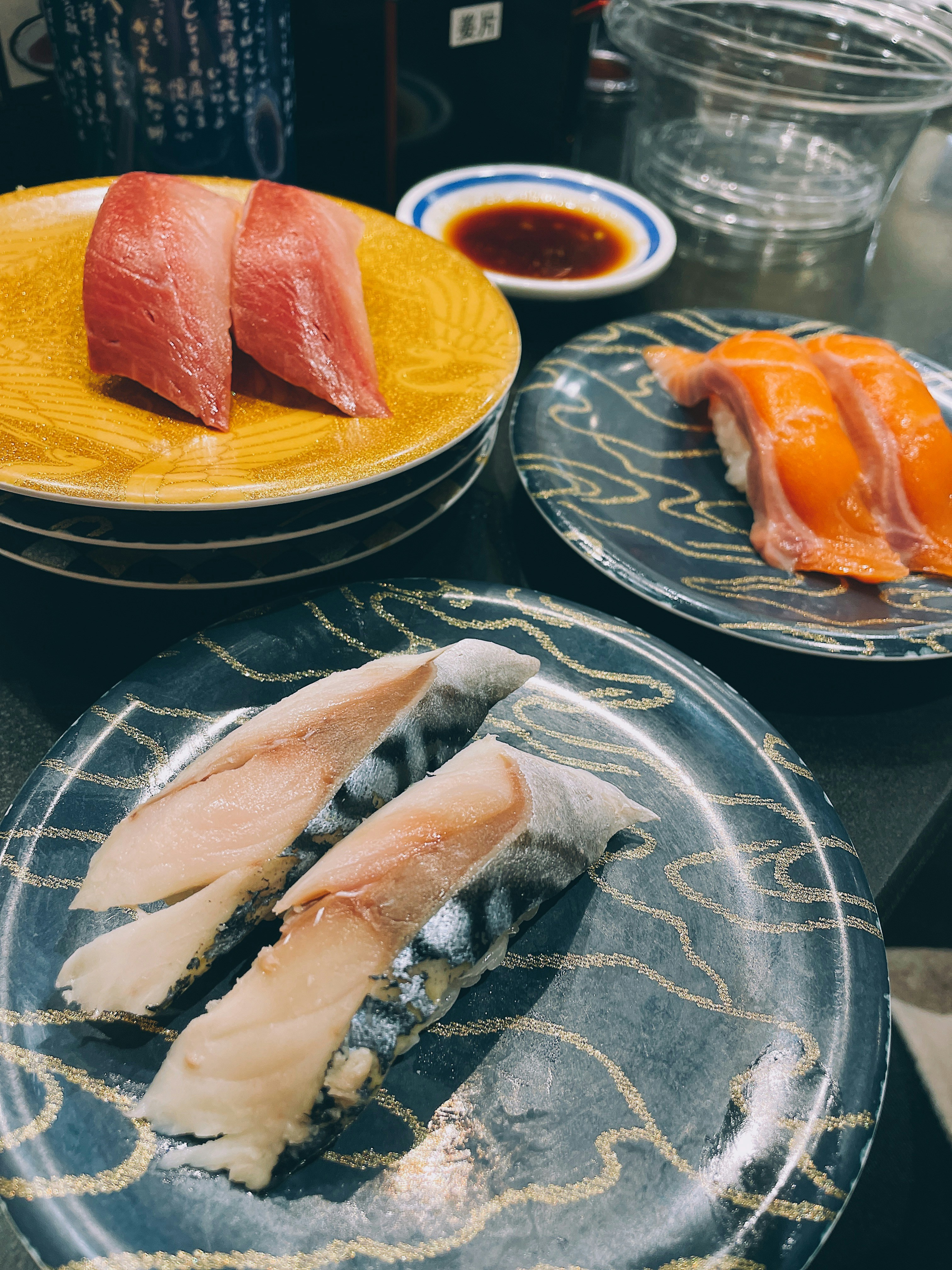 Three plates of assorted sushi with soy sauce.