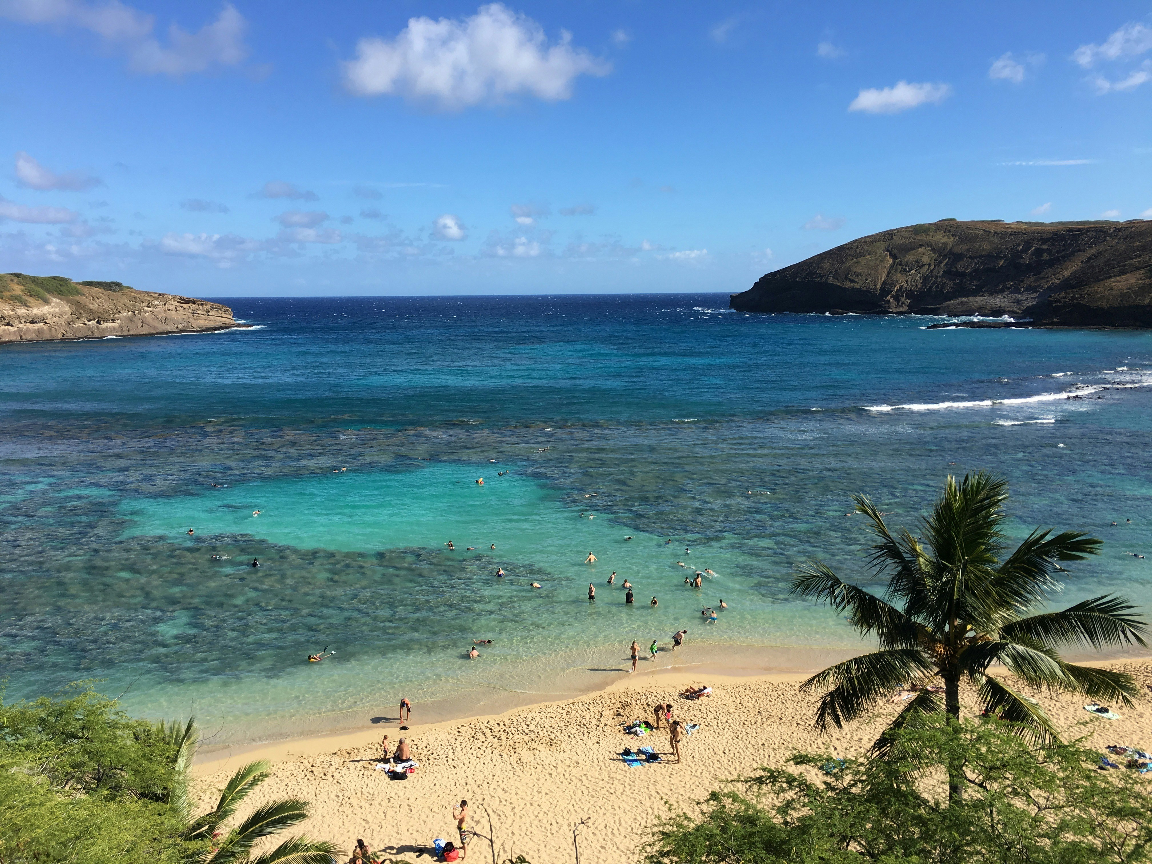 Tropical beach with clear blue water, people, and green hills.