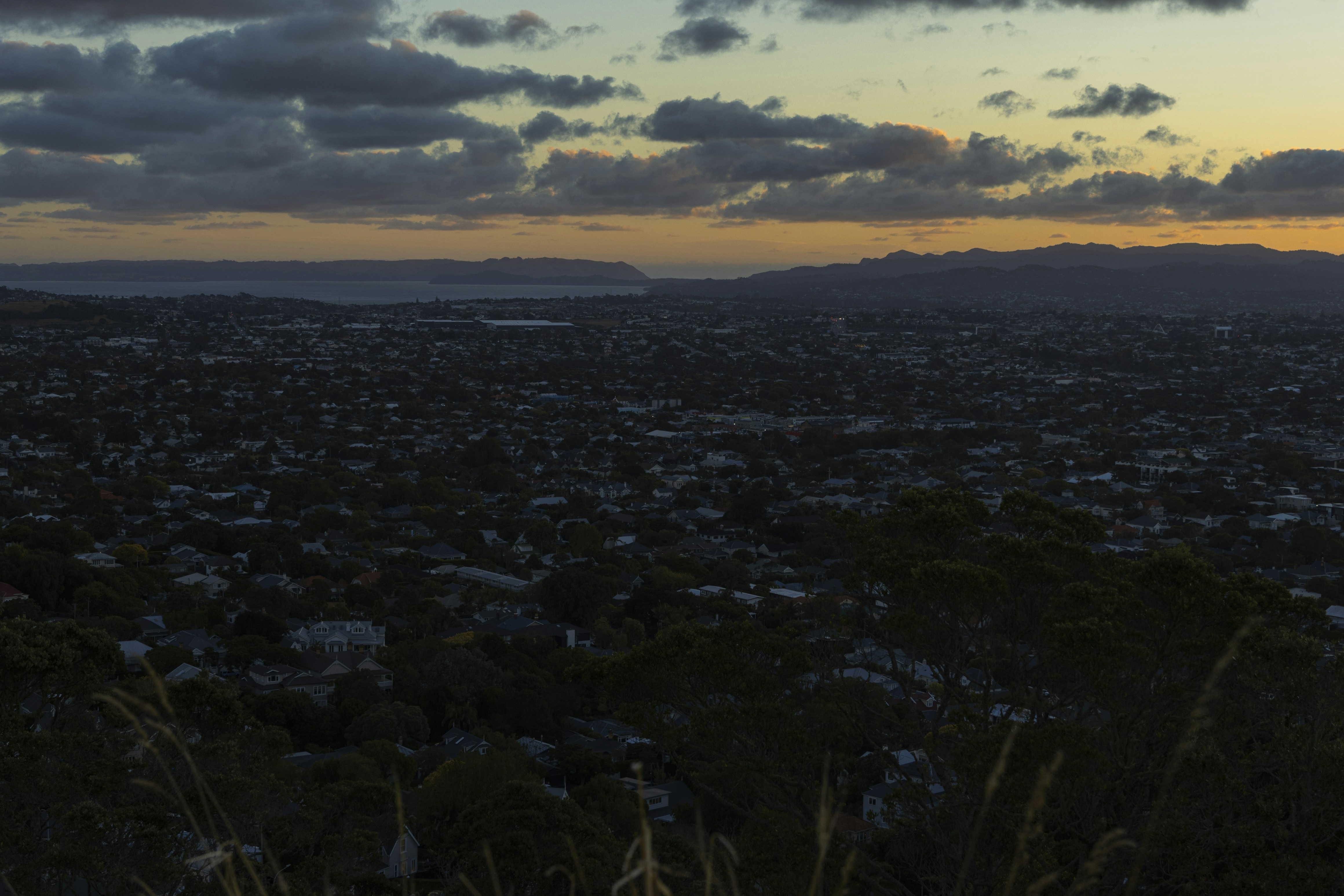 Dark cityscape at twilight with distant mountains and cloudy sky.