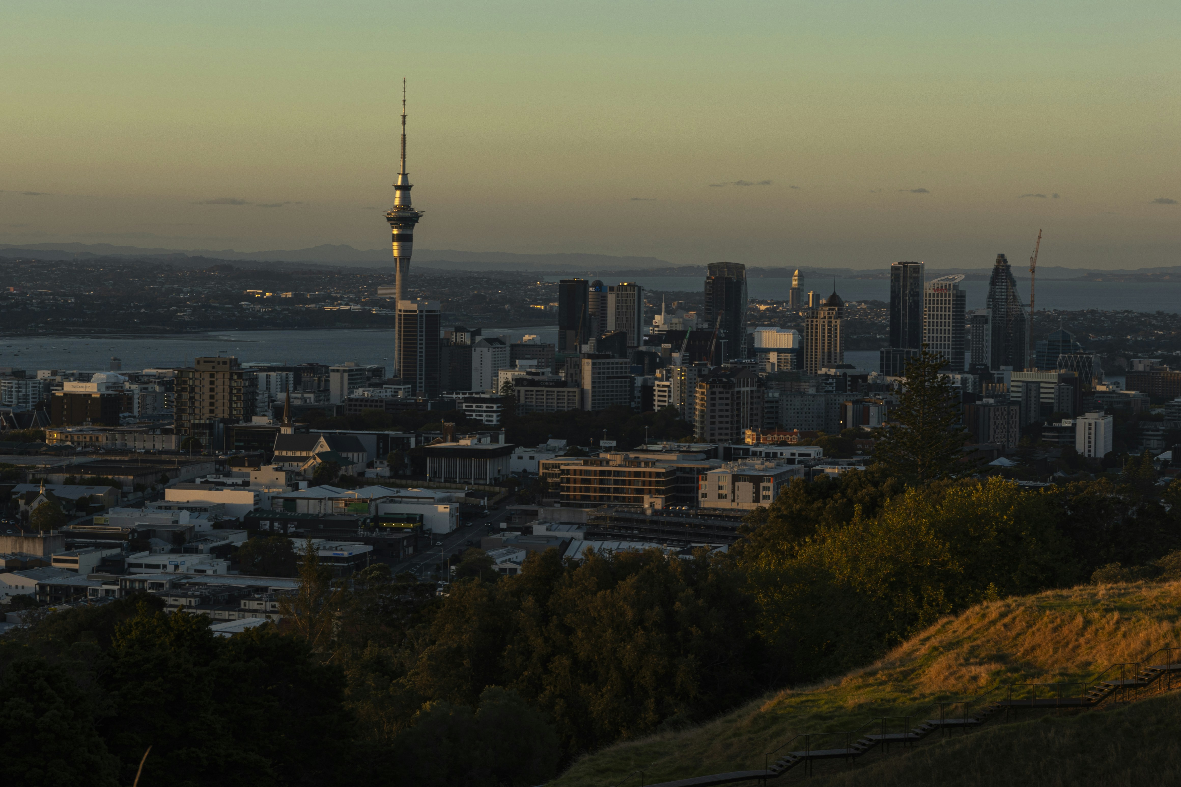 Auckland cityscape with sky tower and harbor at sunset.