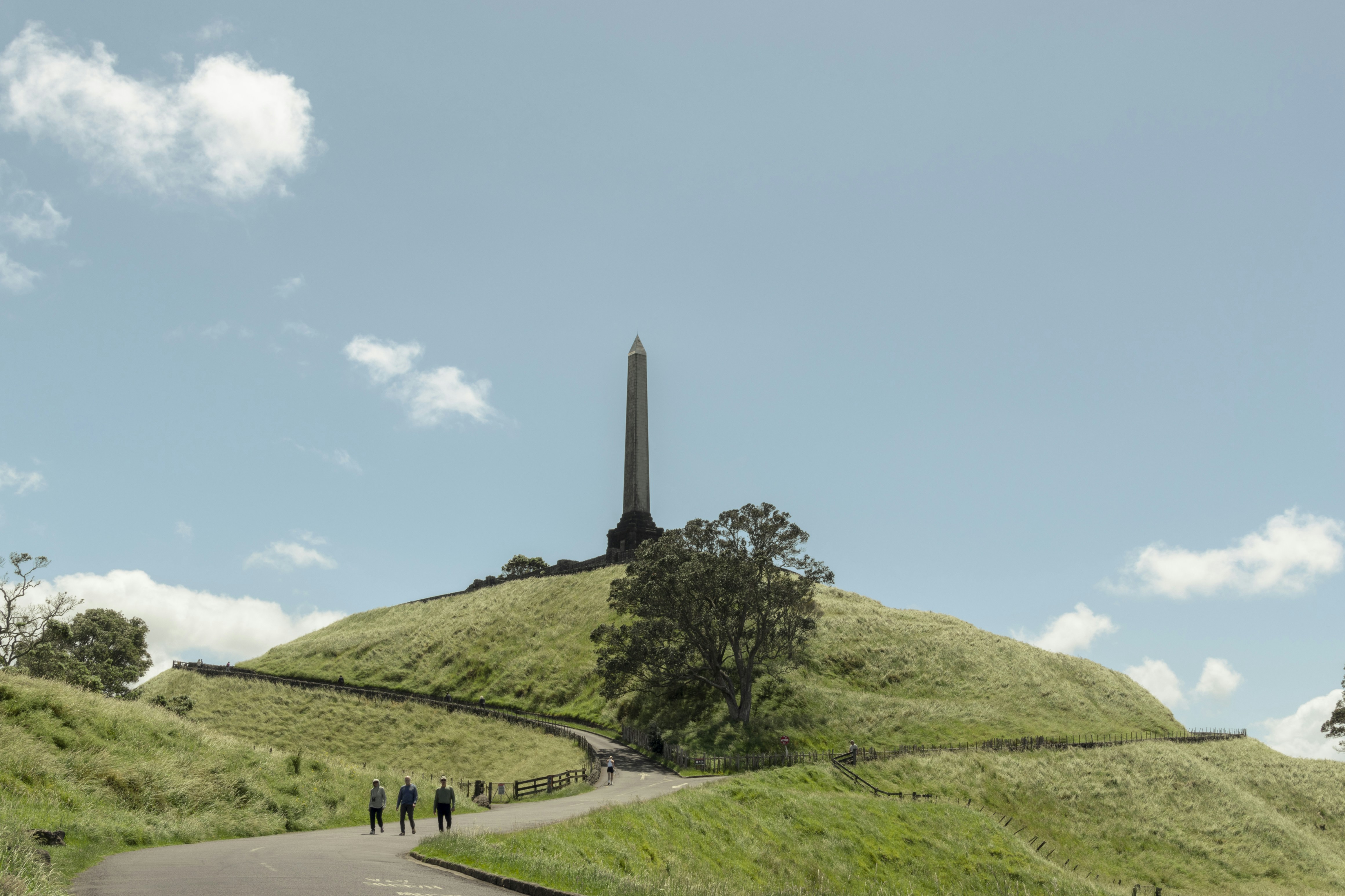 Obelisk on a green hill, winding path, and blue sky.