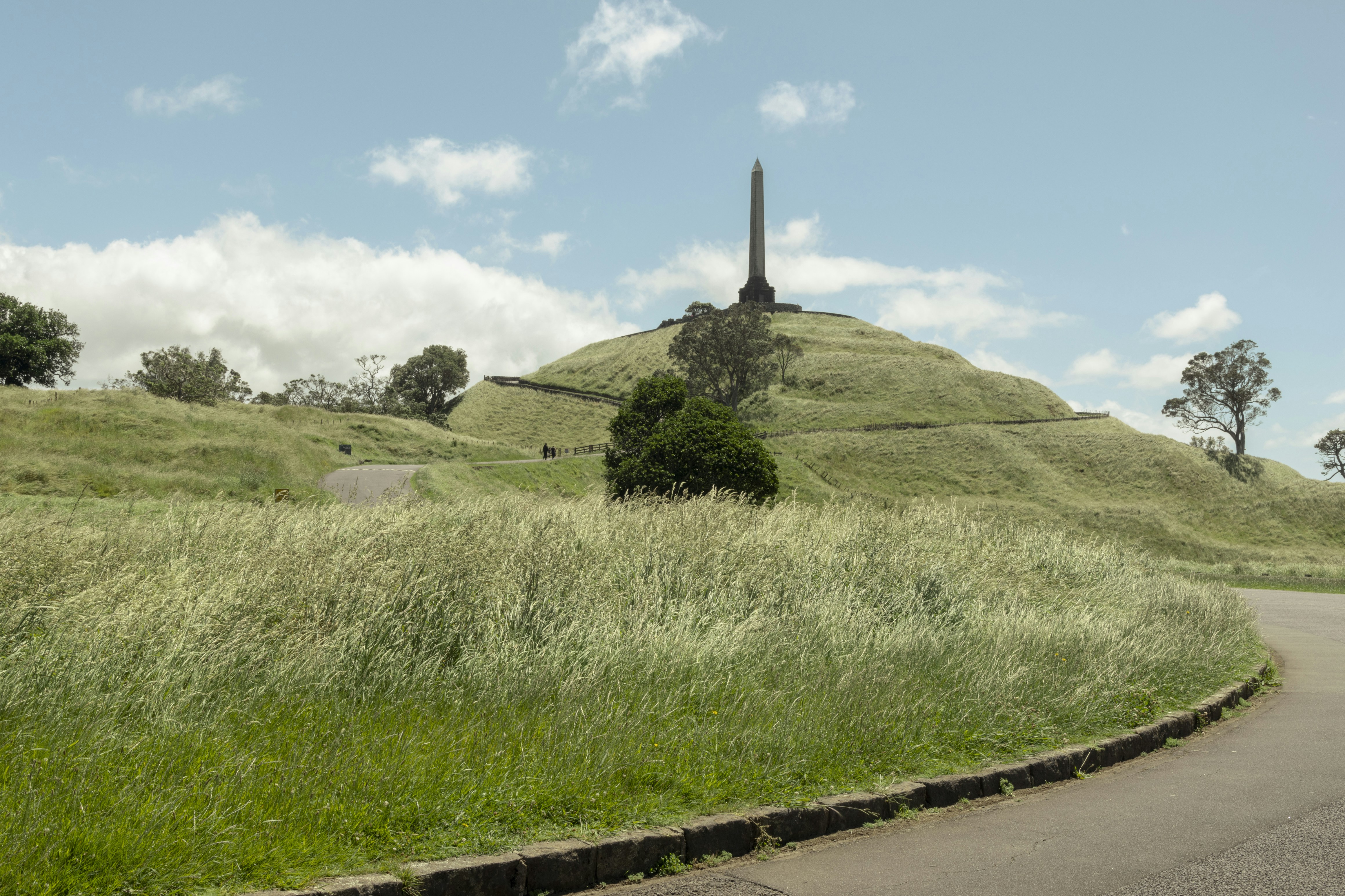 A grassy hill with an obelisk under a cloudy sky.