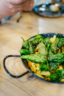 Green padrón peppers and french fries in a black pan.