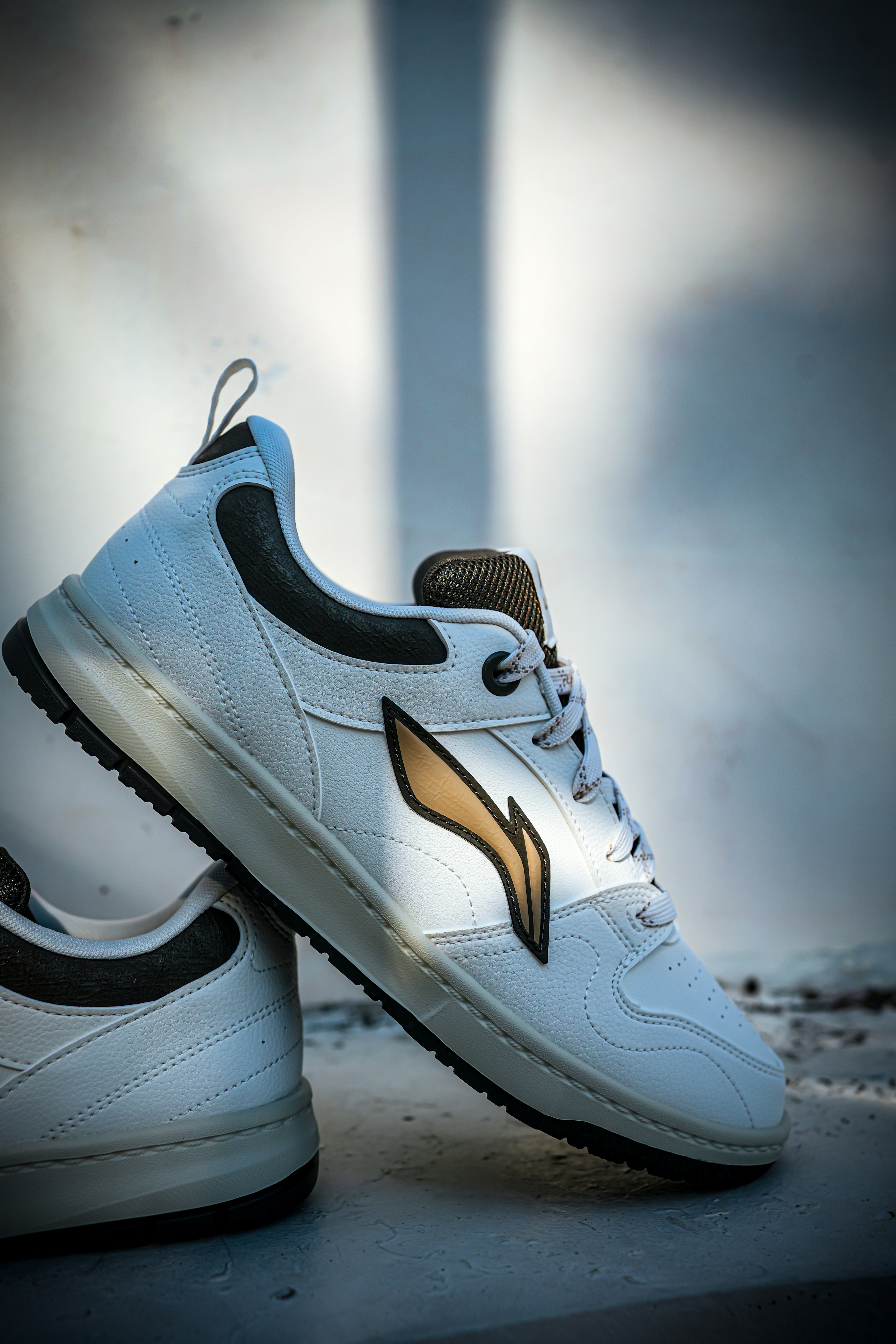 Stylish white sneaker with gold emblem in dramatic lighting.