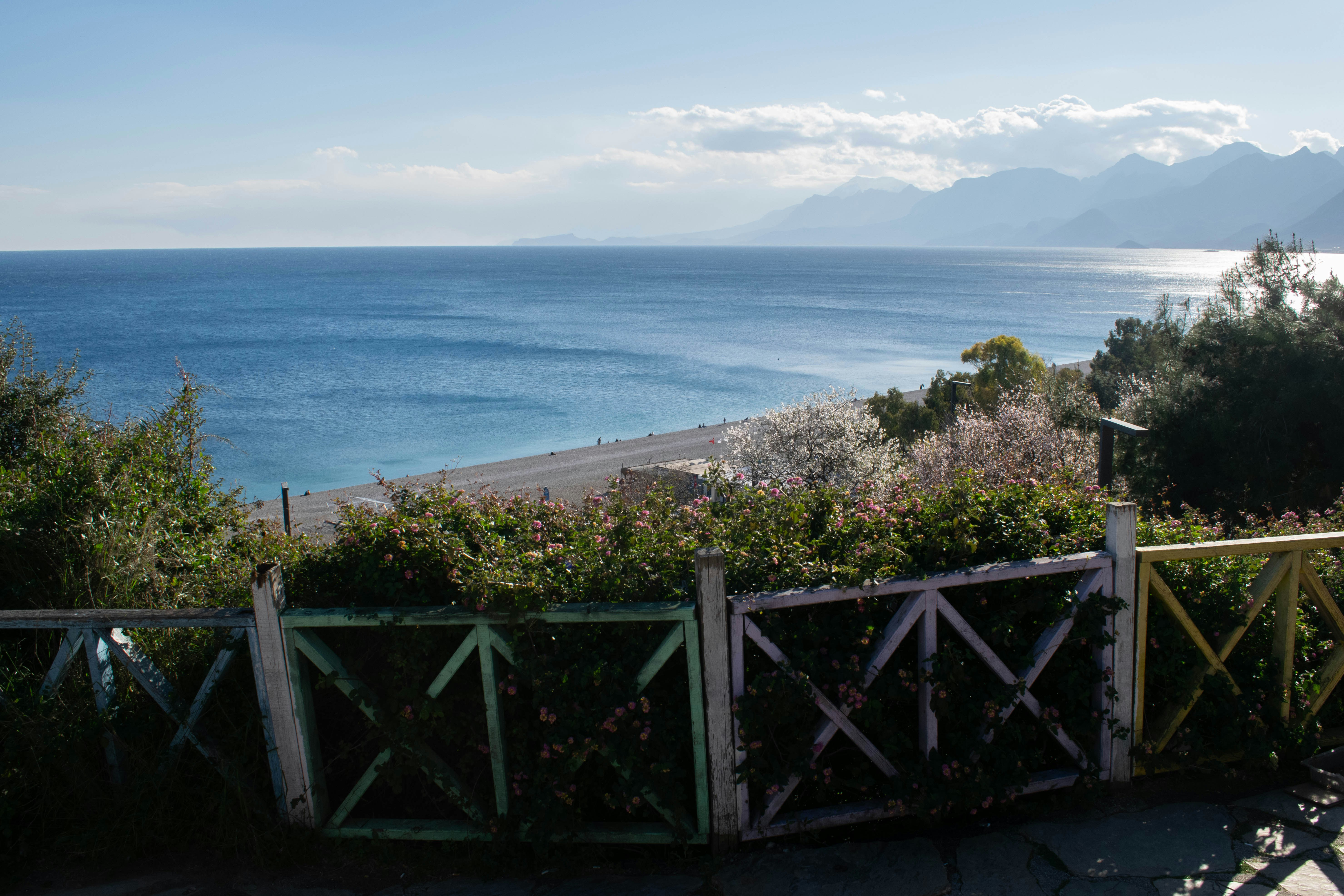 Scenic beach and ocean with distant mountains and a fence.