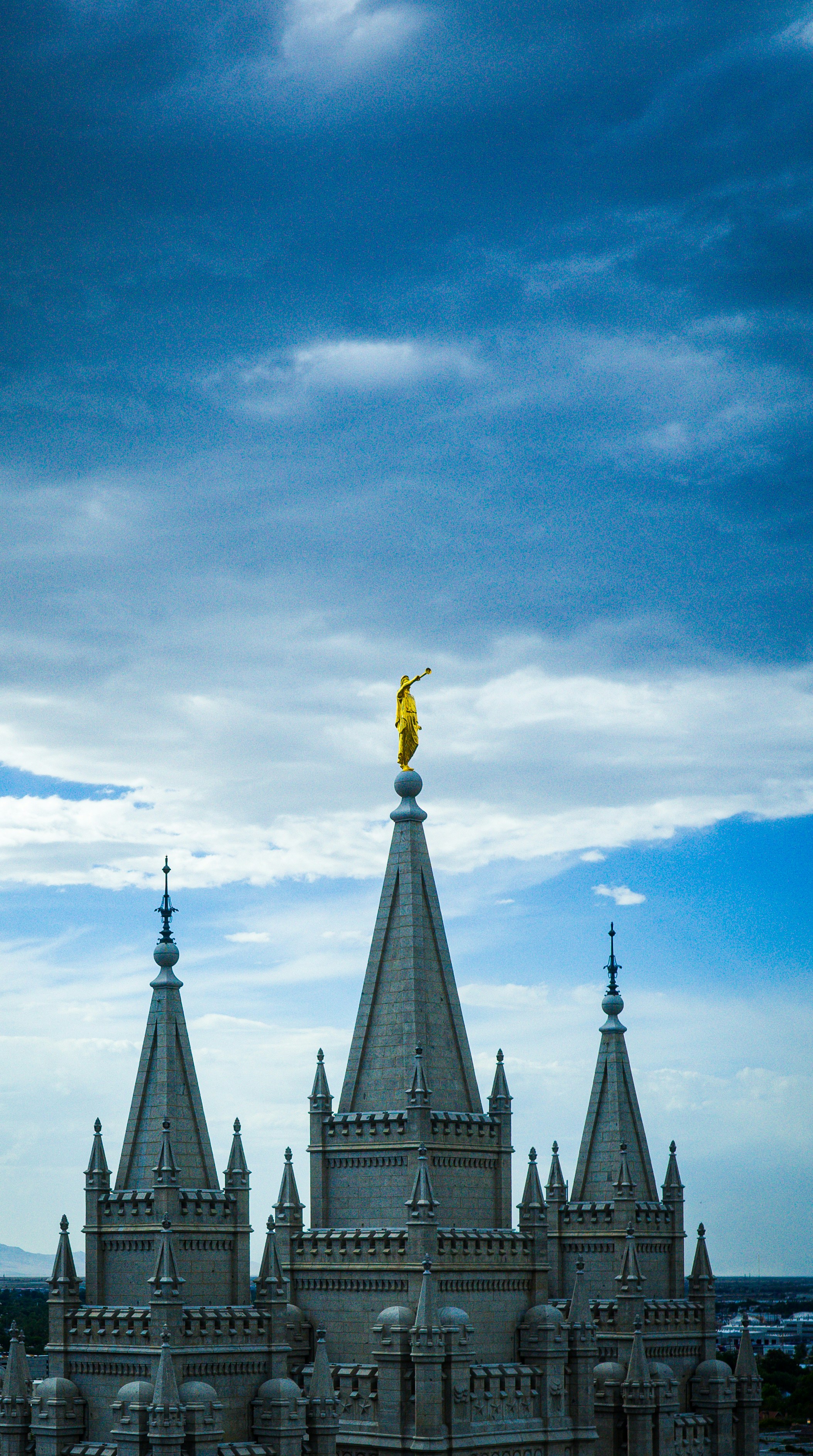 Golden angel statue atop a majestic temple against cloudy sky.