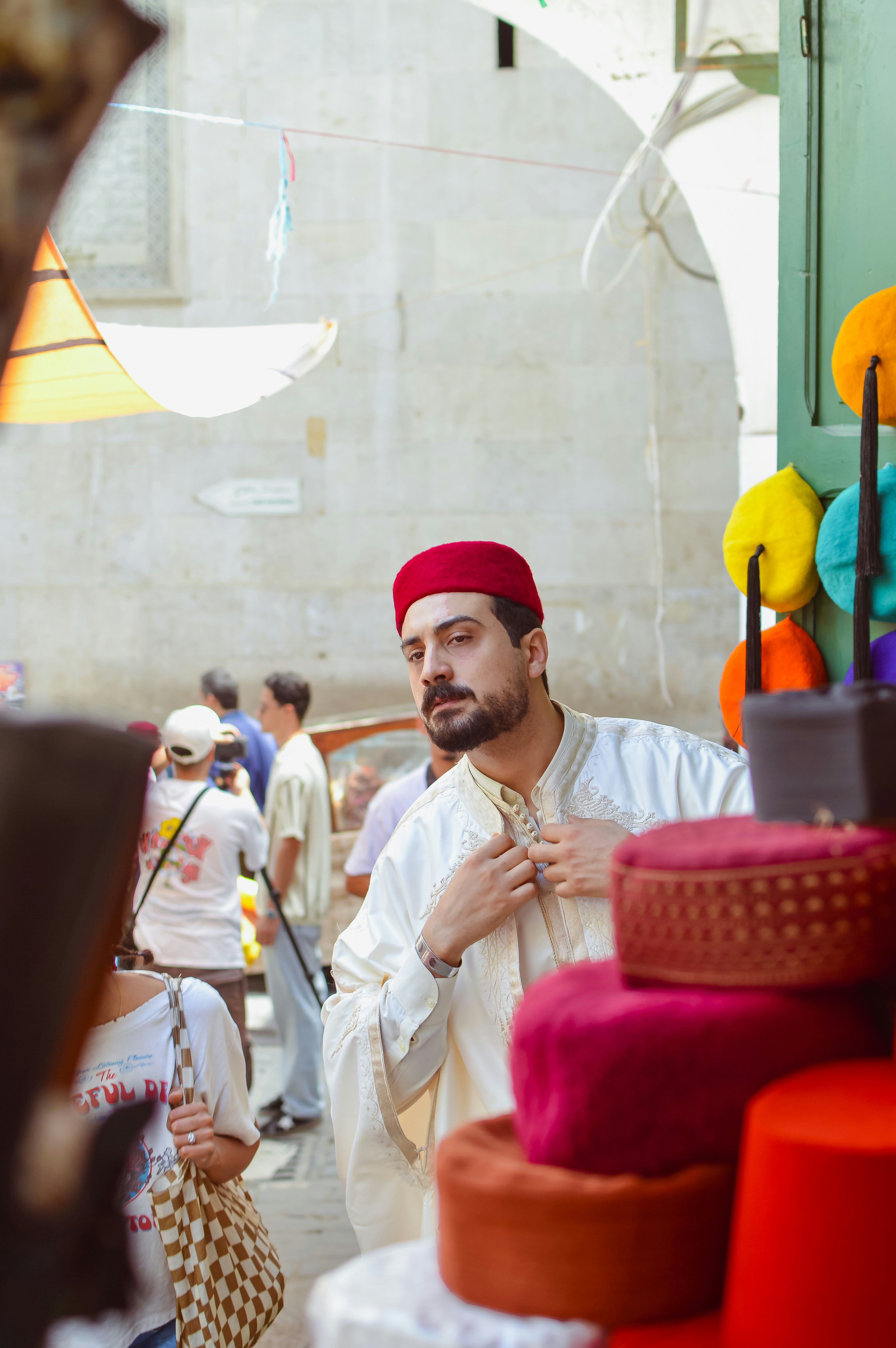 Man in red fez and white robe adjusting clothing.