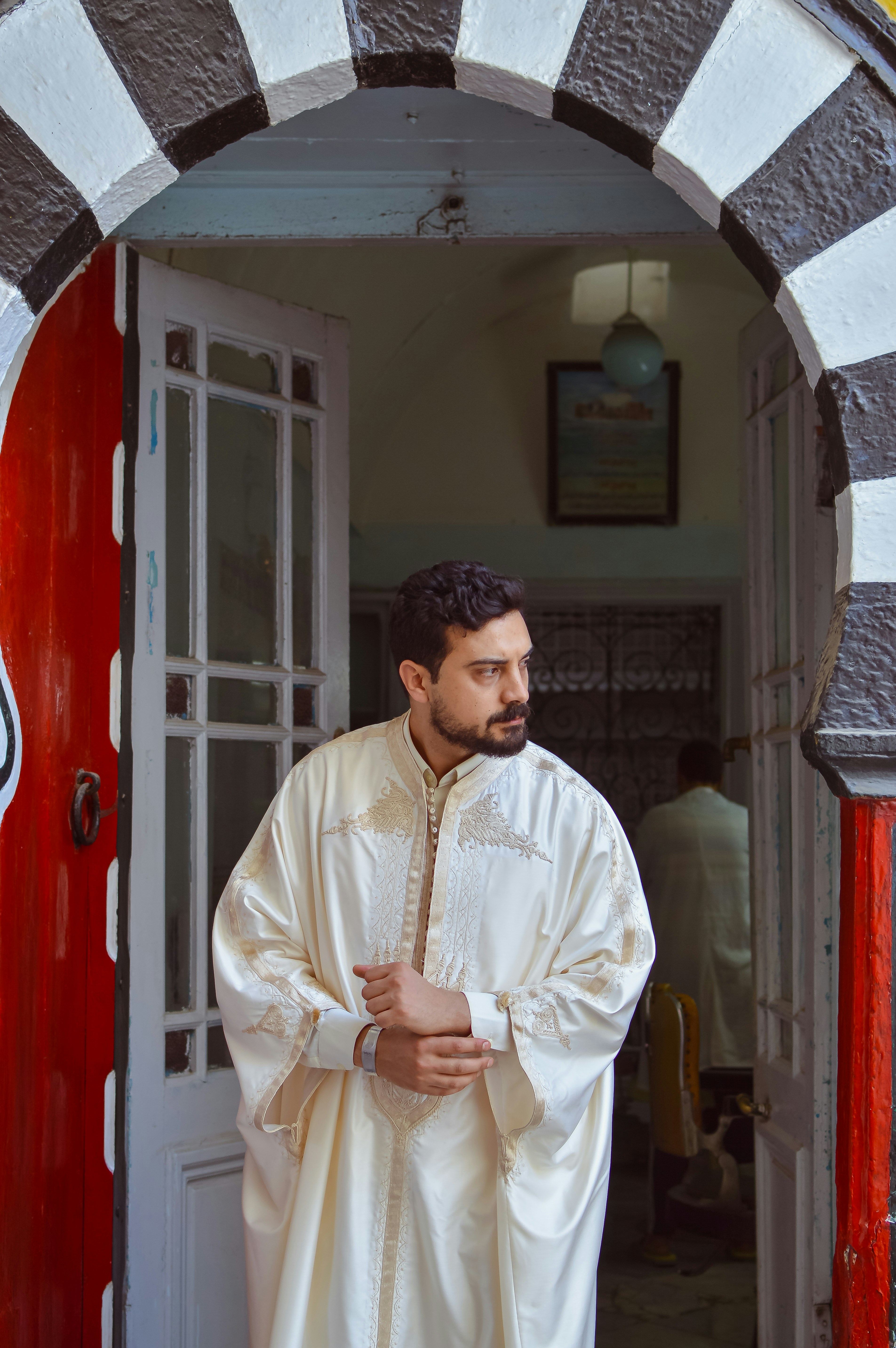 Man in traditional cream robe stands in a decorative archway.