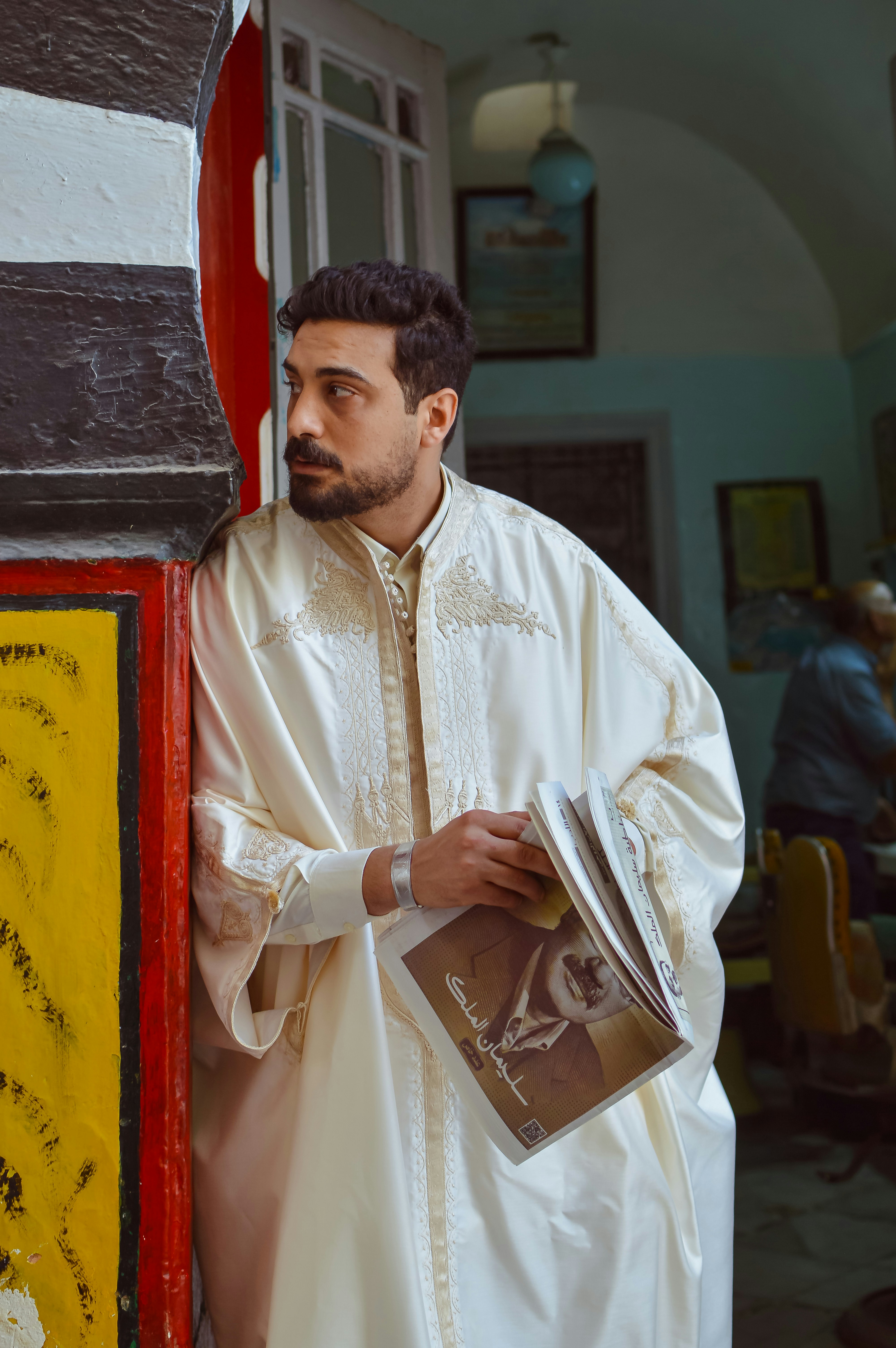 Man in traditional white robe holding a magazine.
