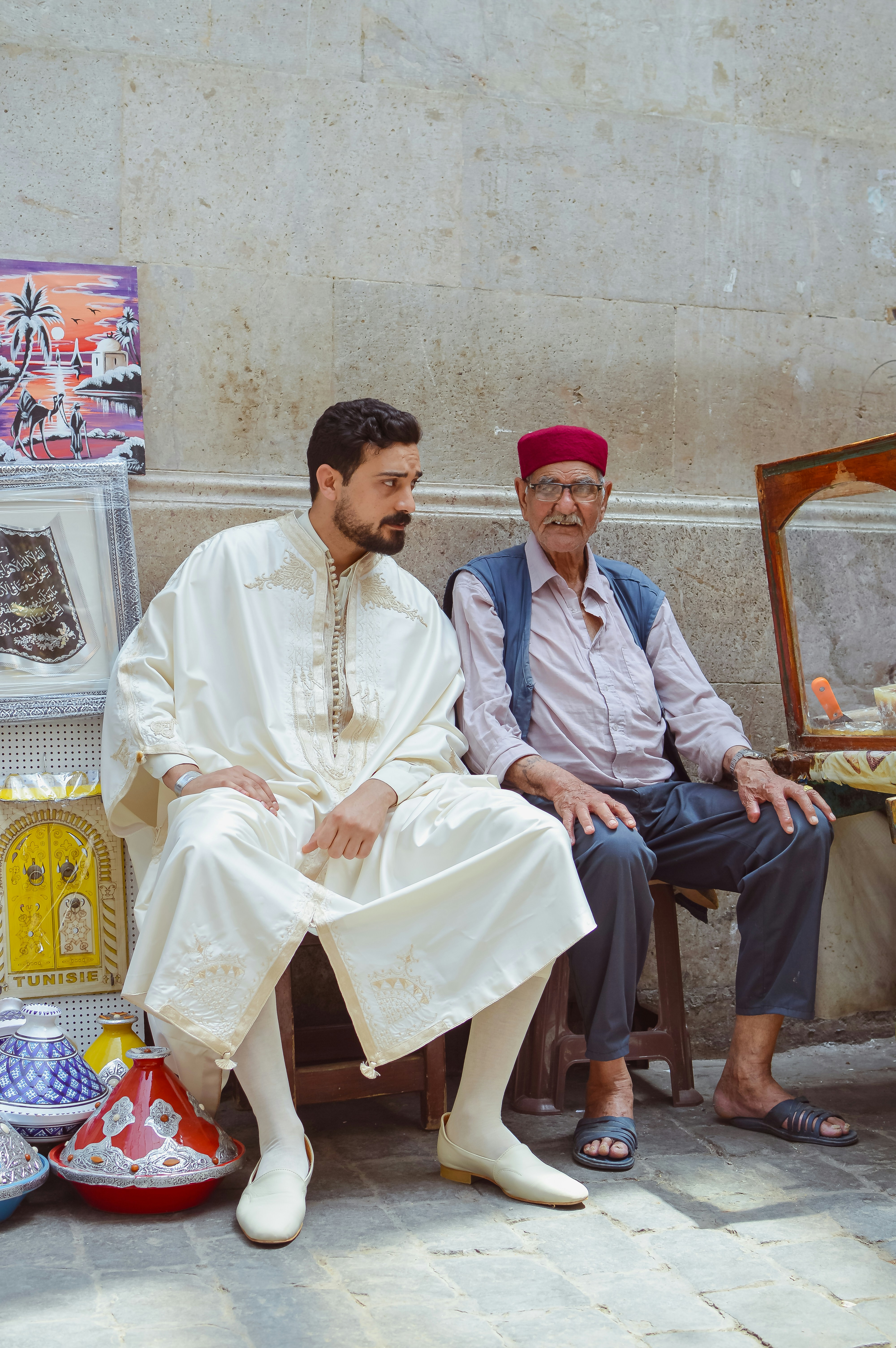 Two men in traditional attire sit on a street.