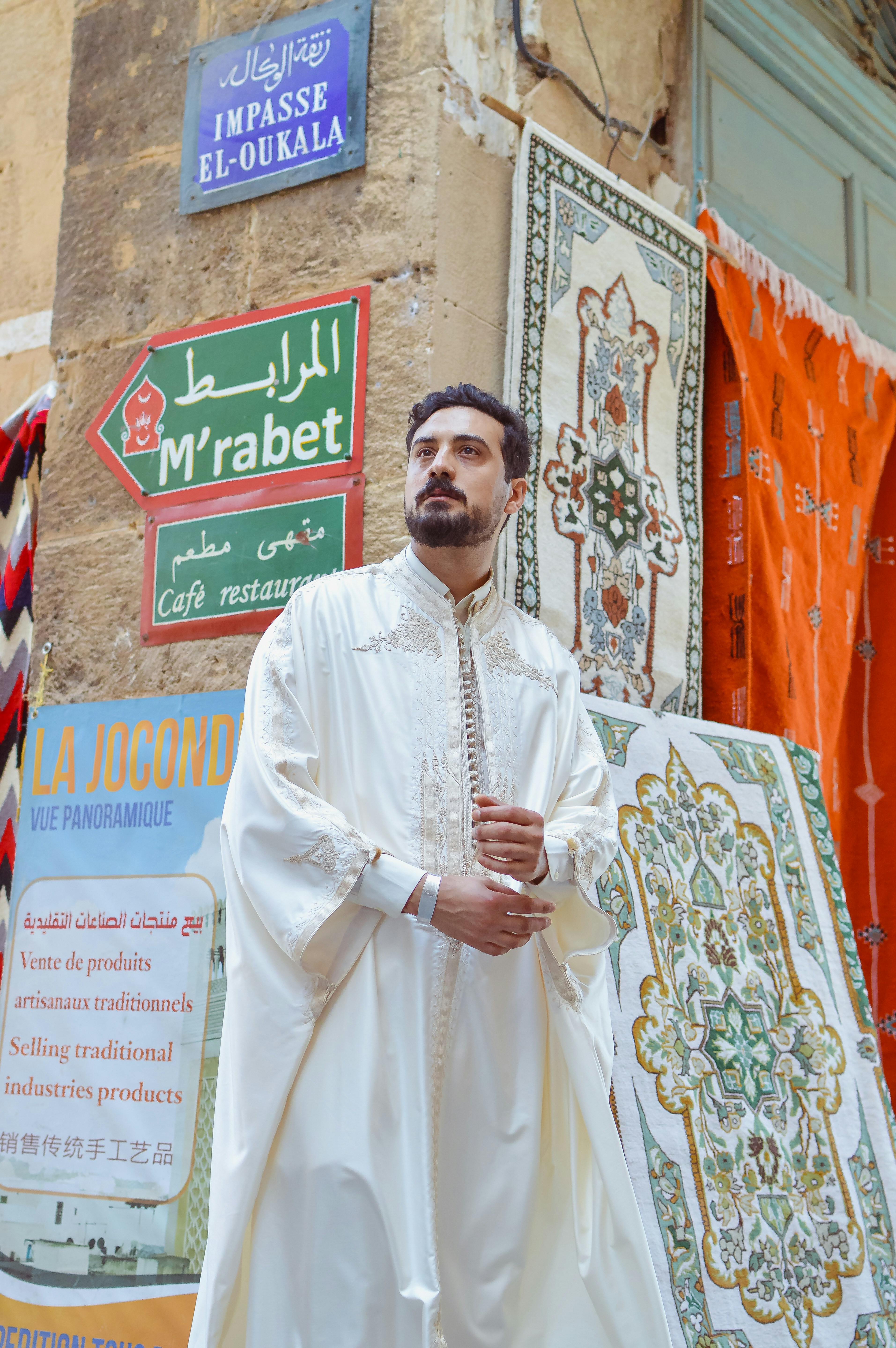Man in white traditional attire on a street with signs.
