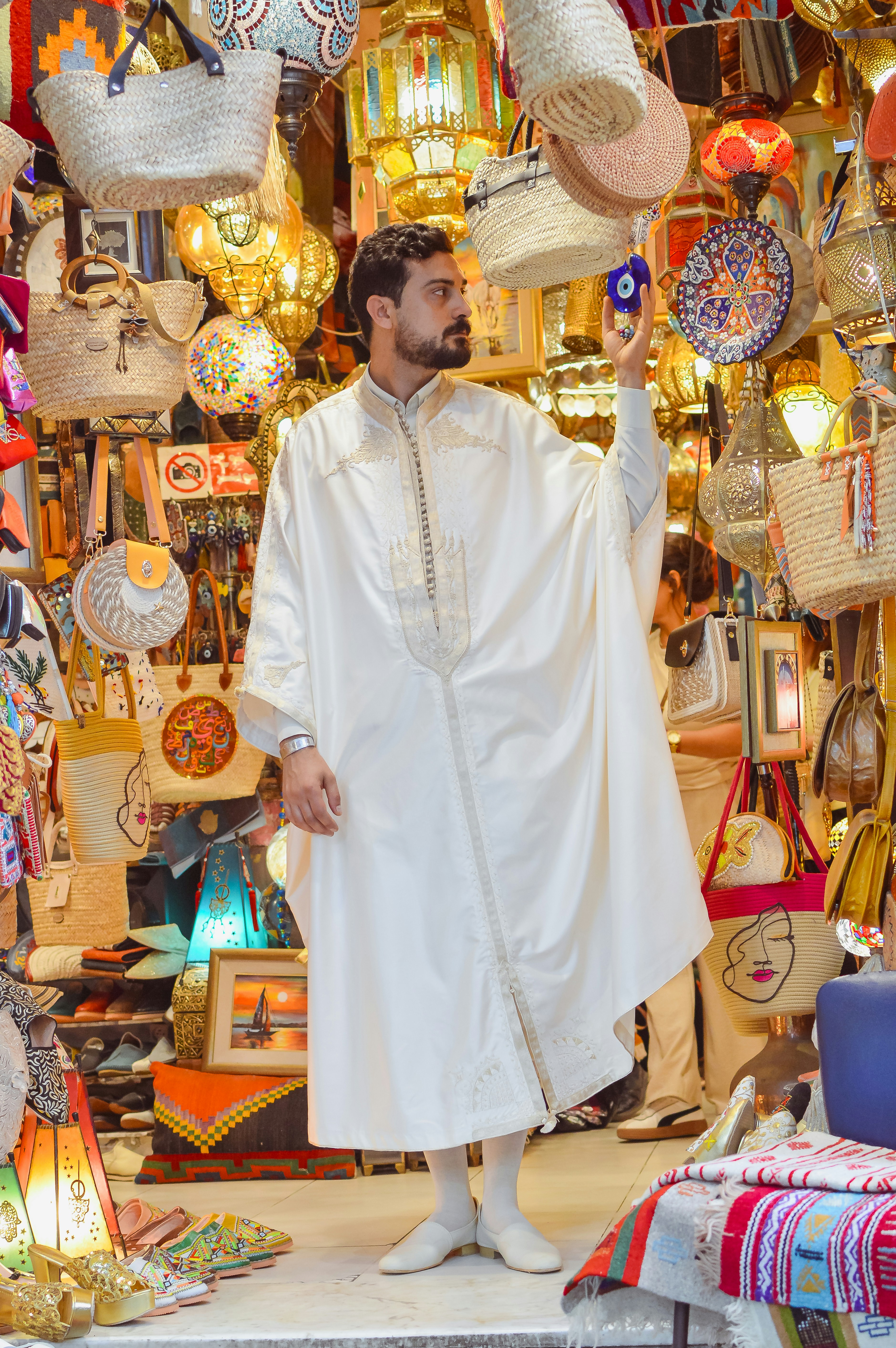 Man in white robe holding charm in a vibrant market.