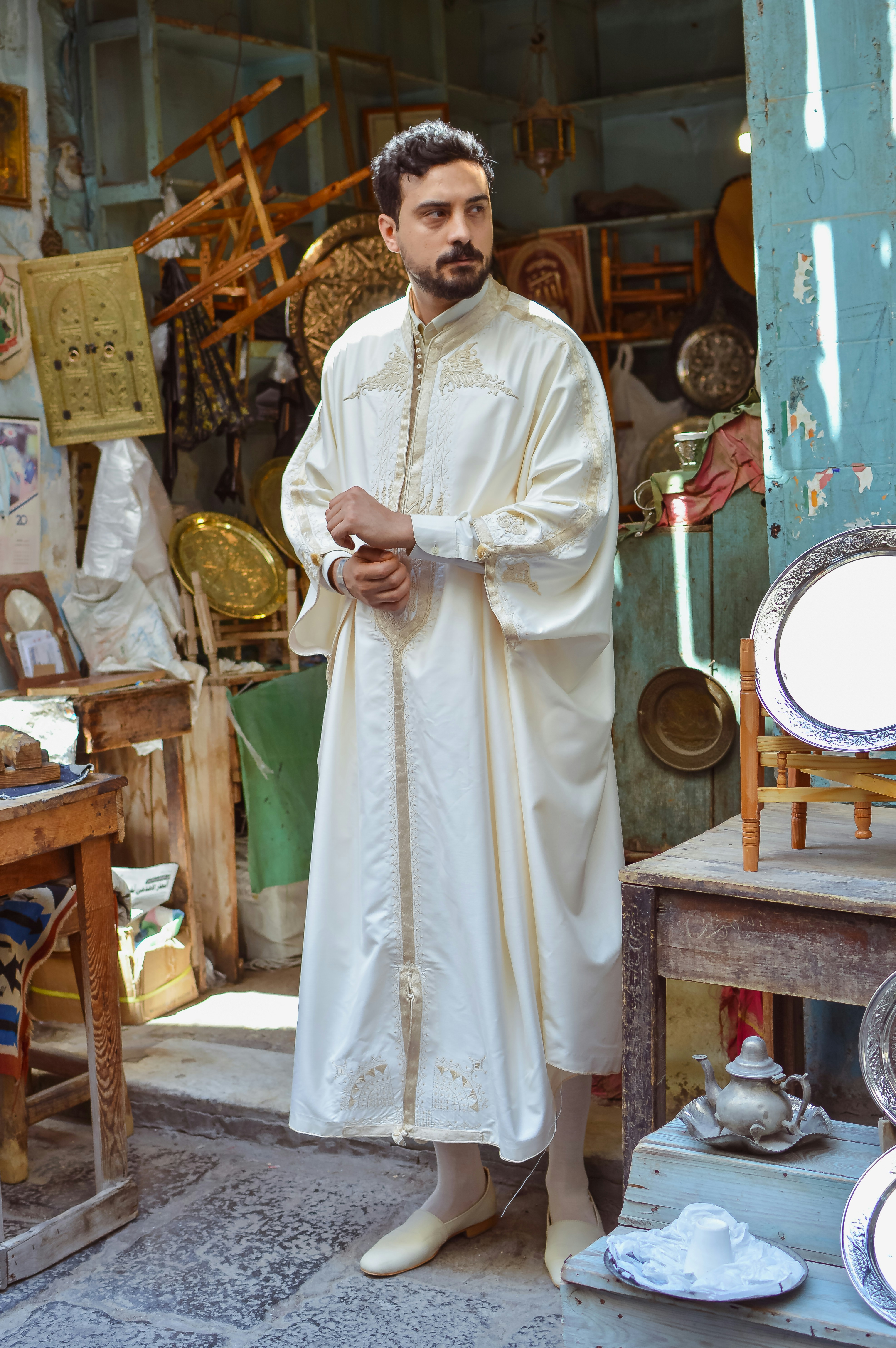 Man in embroidered white robe stands in a traditional shop.