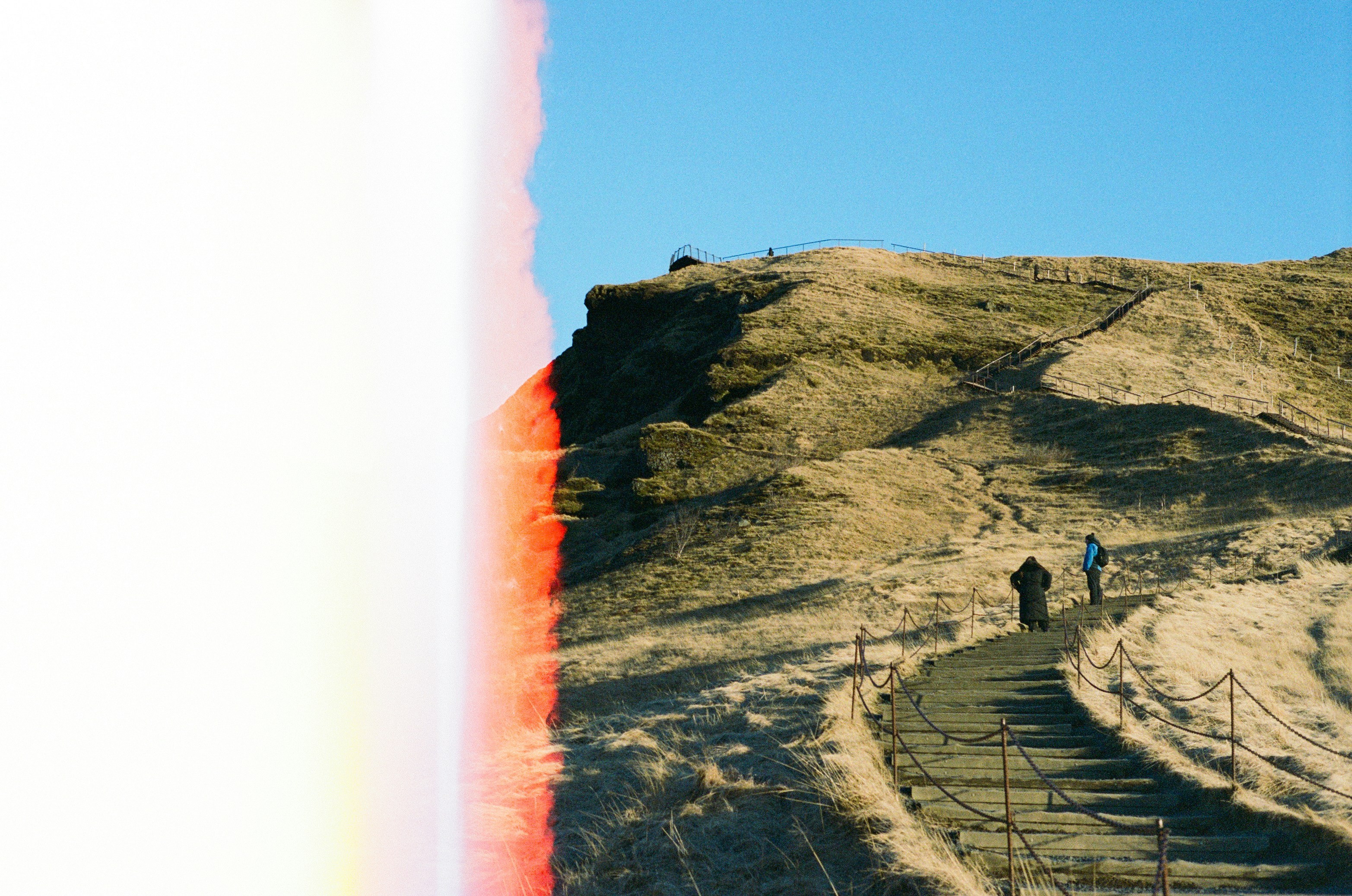 People walking on a winding path up a grassy hill.